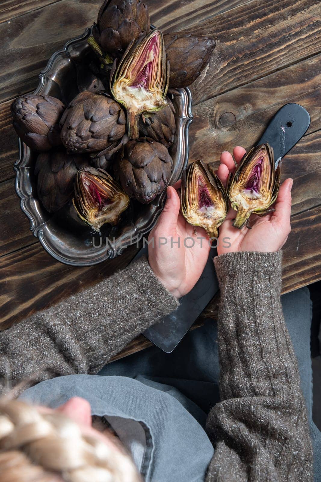Woman cleaning fresh artichokes and cooking on wooden table, rustic still life top view,concept of healthy eating and fine dining,