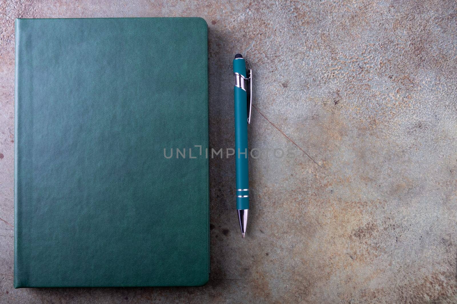 A green bound notebook on a light brown, textured surface, accompanied by a blue pen