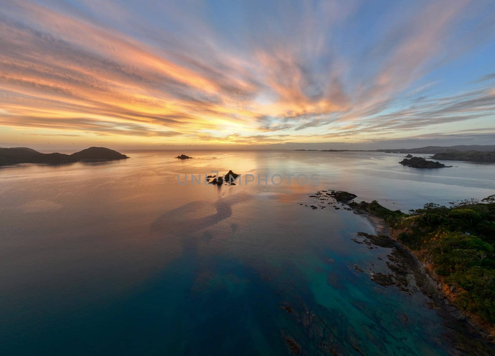 Beautiful clouds obscuring the sun rising over the beach town of Oakura, New Zealand. Silhouetted rocky islands and outlets frame the serene and tranquil scene