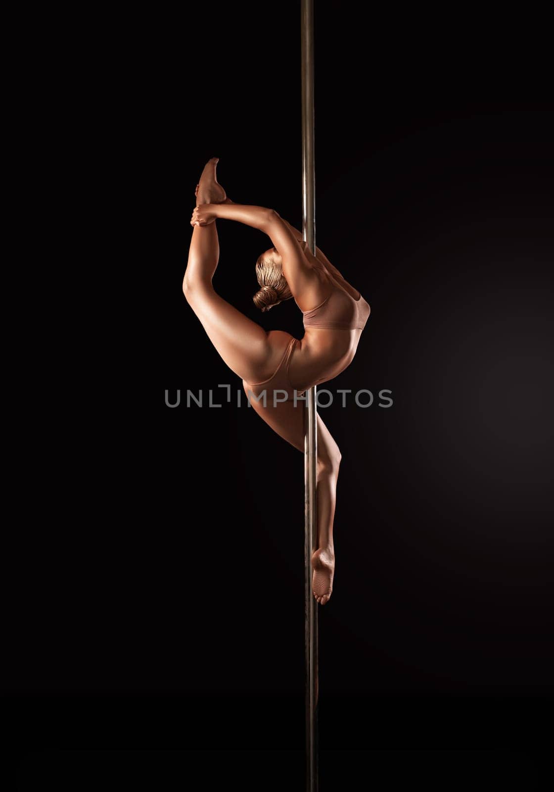 Side view of flexible slim female in underwear dancing sensual dance around pole on black background