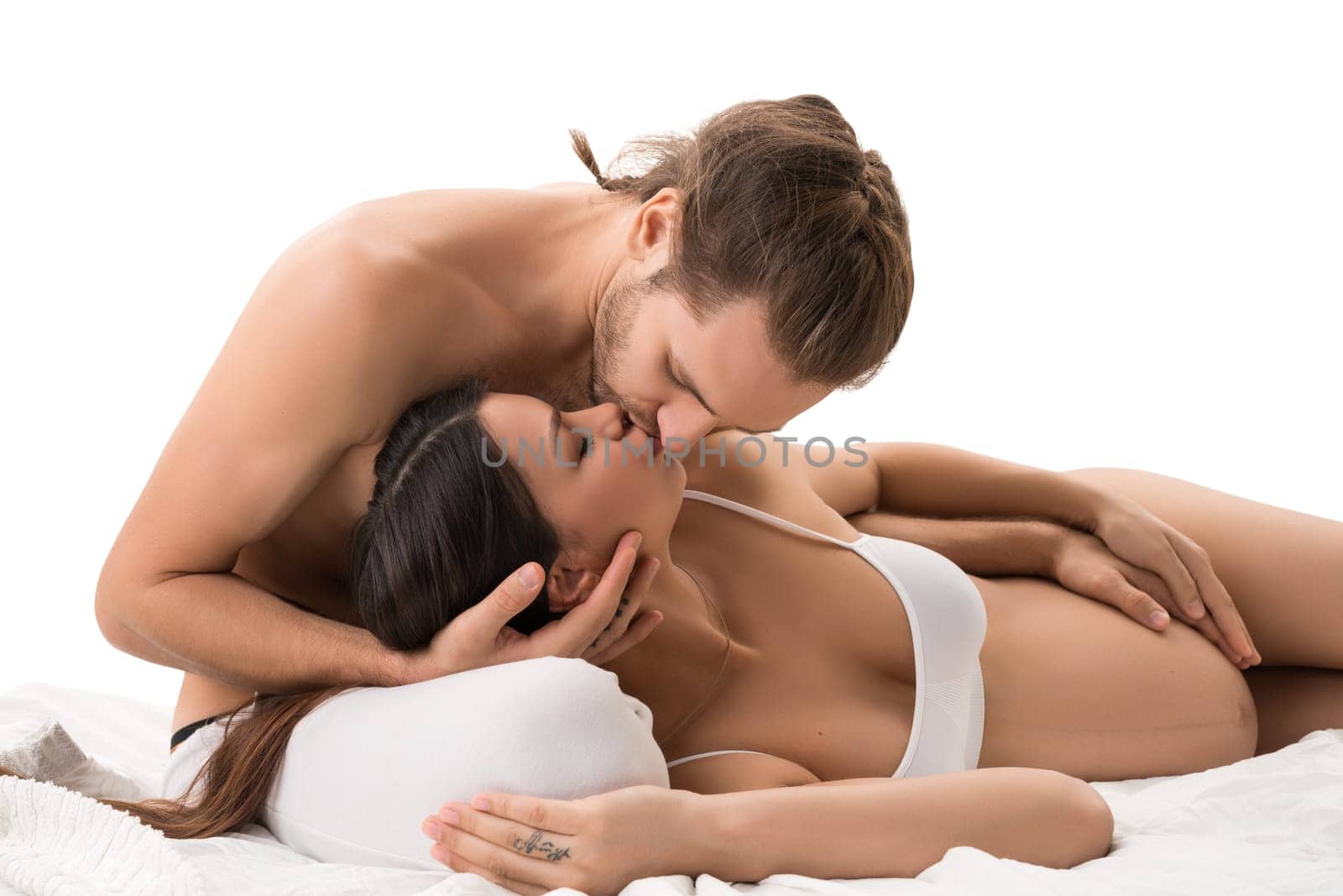 Happy family with pregnant mother embracing and kissing in bed isolated shot