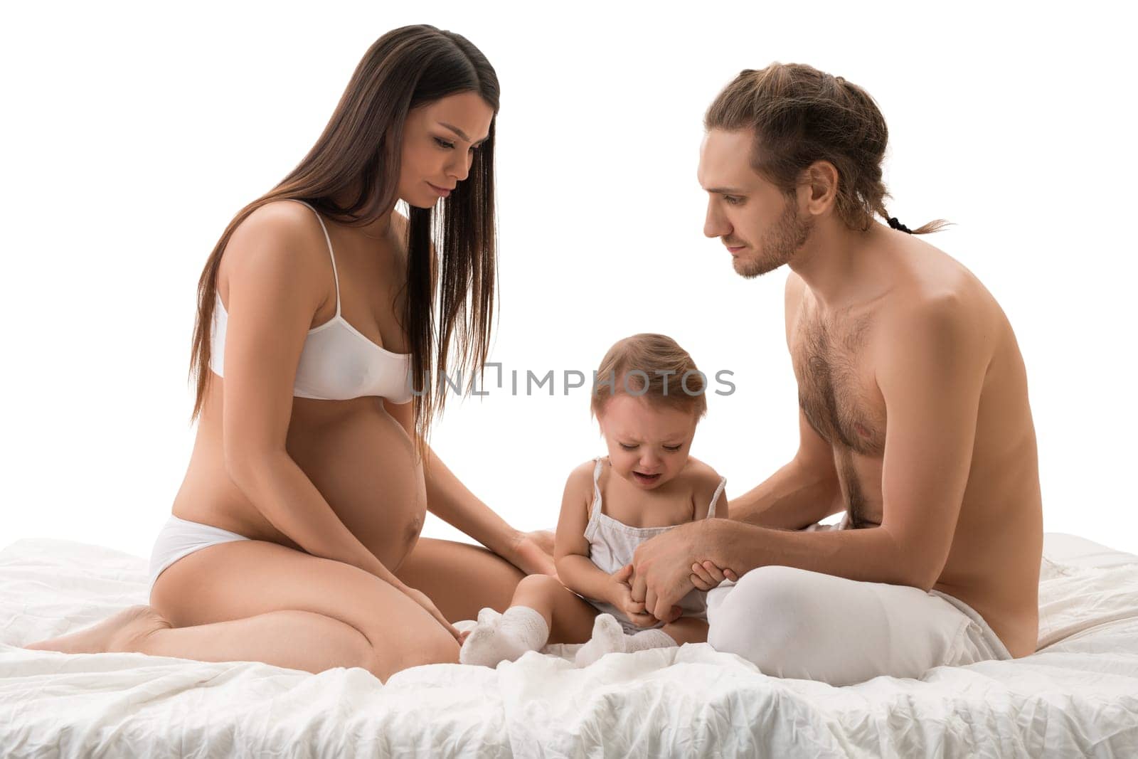 Family shot sitting on bed with their little son, father and pregnant beautiful mother isolated view