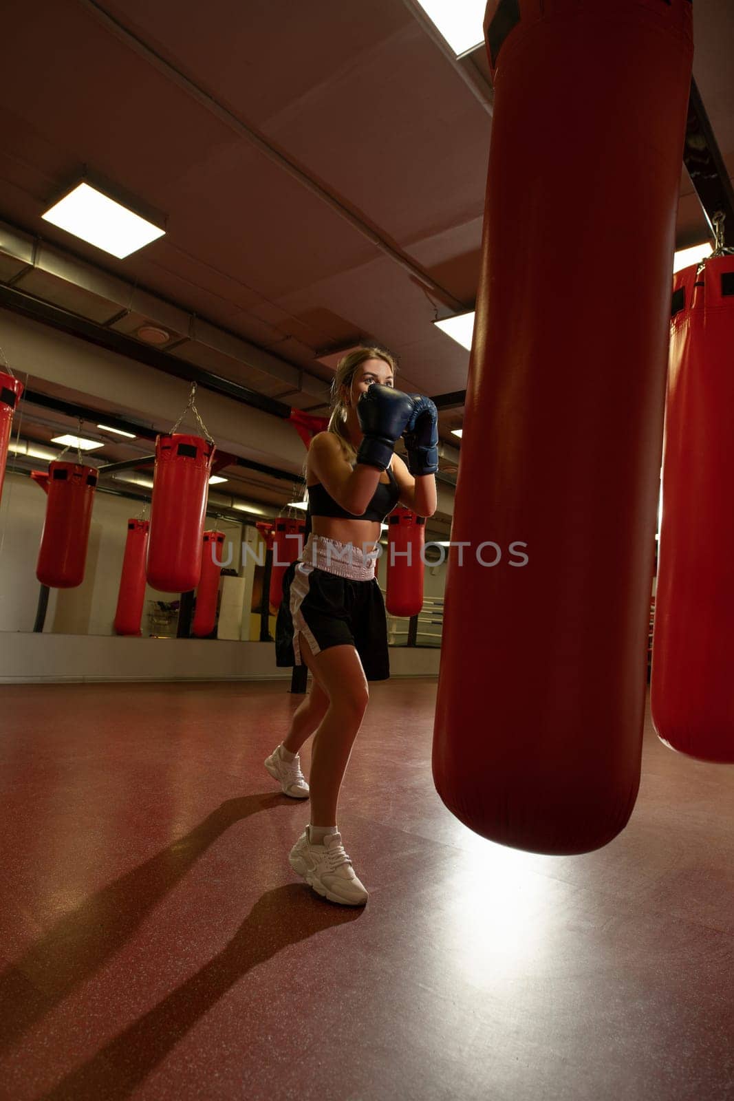Young blonde in boxing gloves exercising with a punching bag in a gym