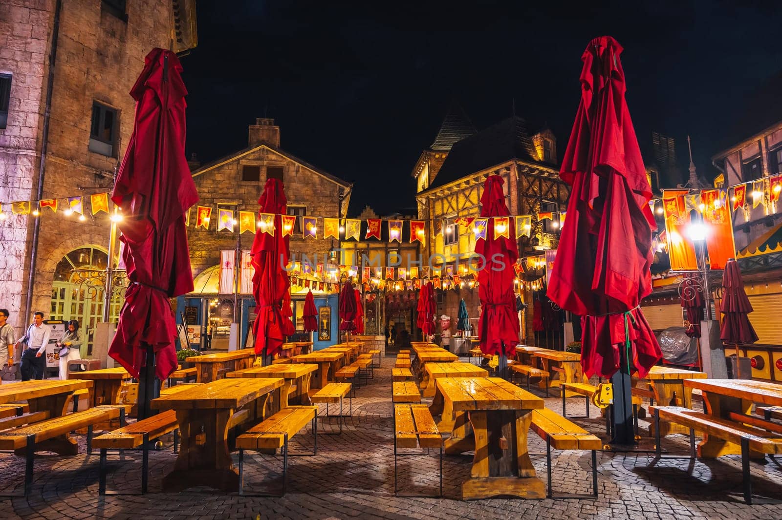 Decorated interior of the festive outdoor cafe street restaurant with wooden tables and benches in night in Ba Na Hills Park. Da Nang, Vietnam - September 13, 2024