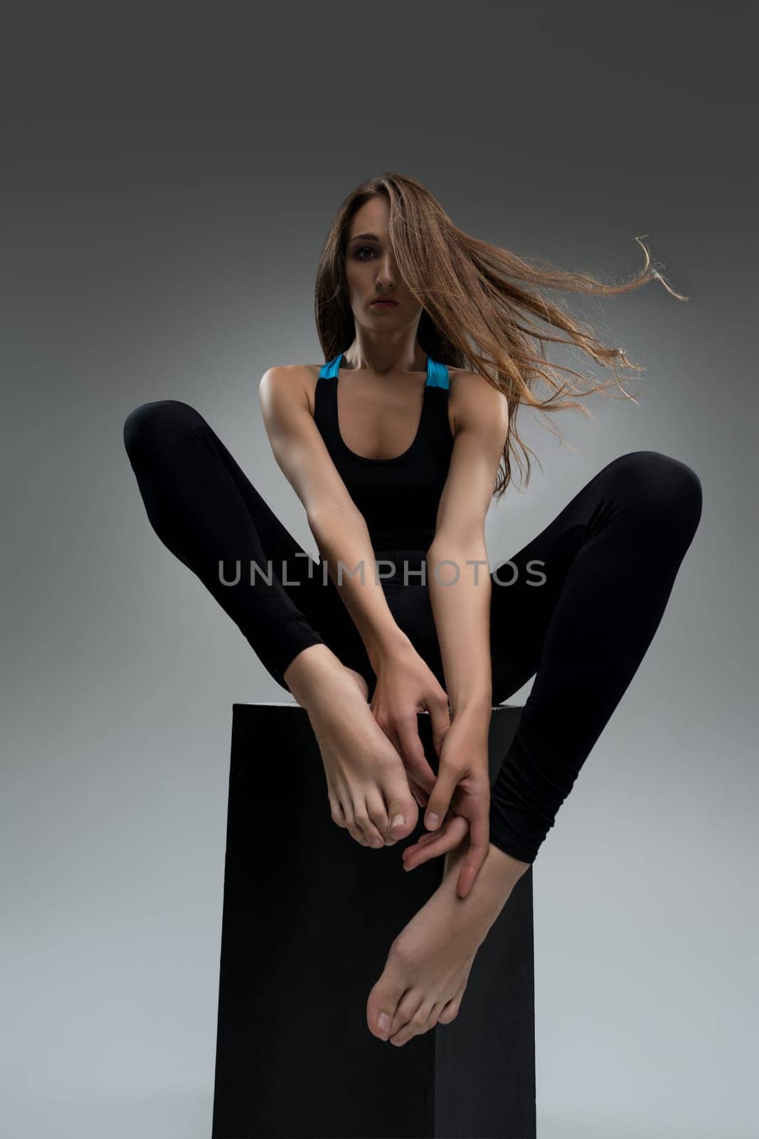 Well-shaped blonde in black sportswear sitting on the cube in the dark room view