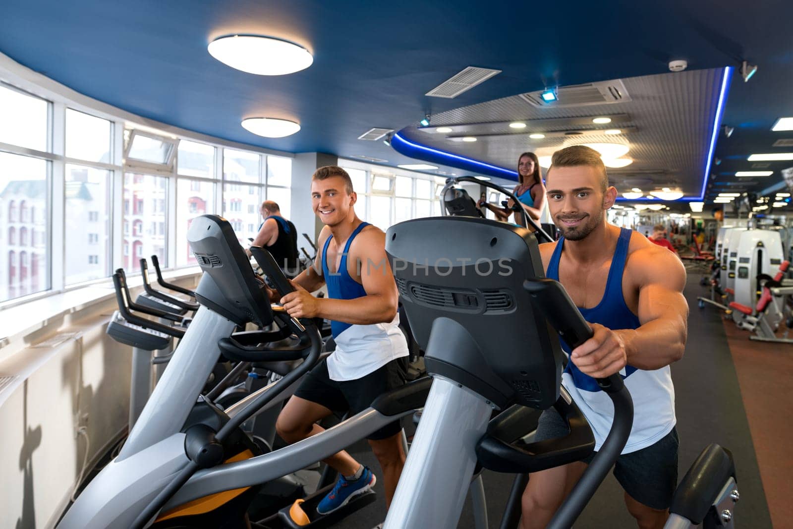 Young sporty males and woman exercising on simulators in a gym