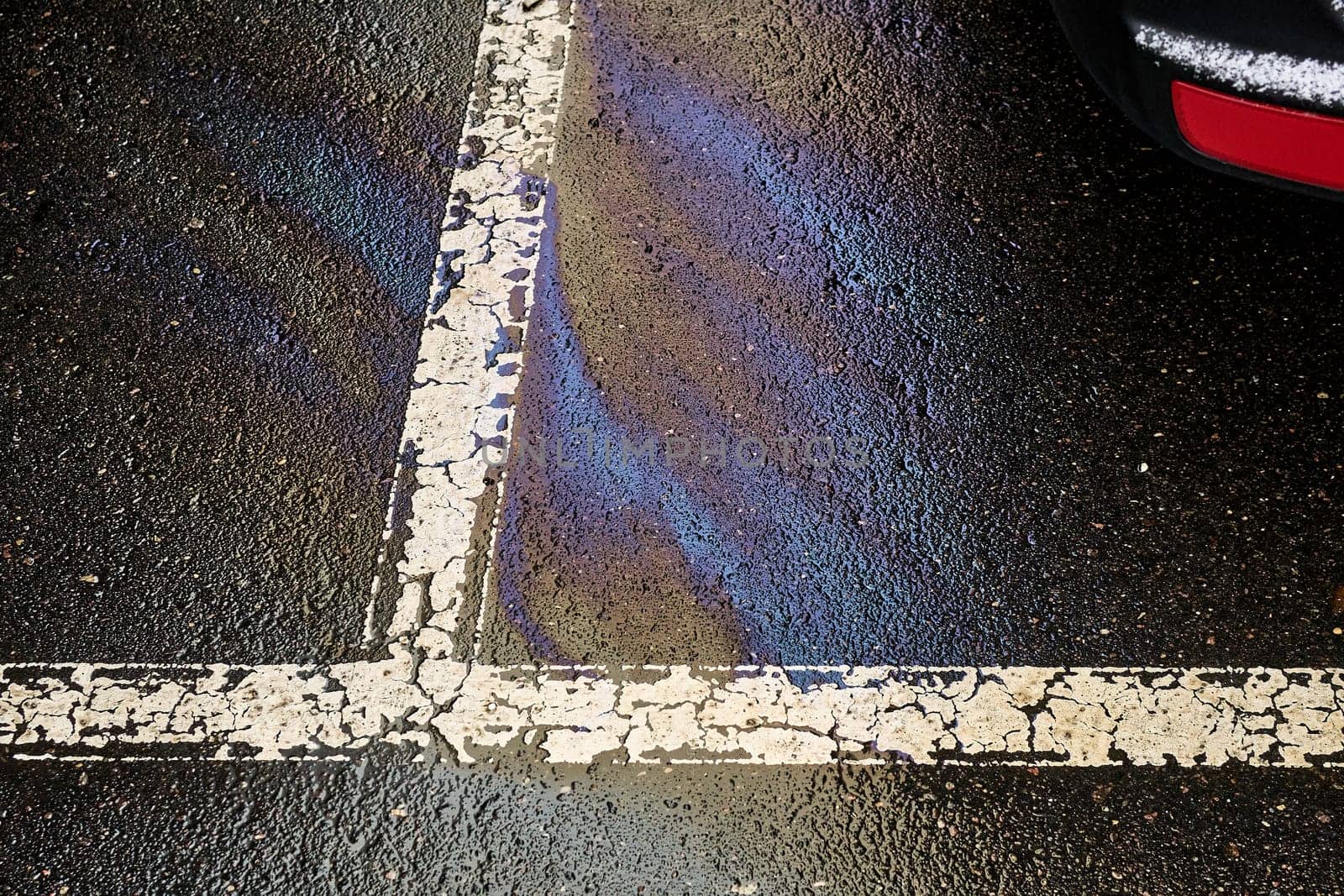 Fuel or oil stain on wet parking lot asphalt, indicated by a white line.