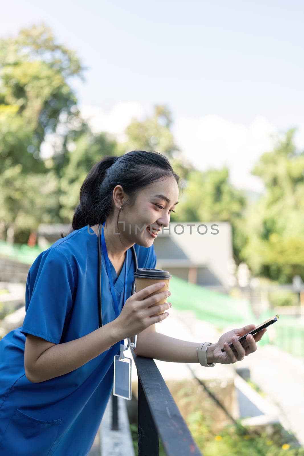 A nurse takes a break sipping coffee and checking her phone embodying a balance of work and leisure in a serene outdoor environment.