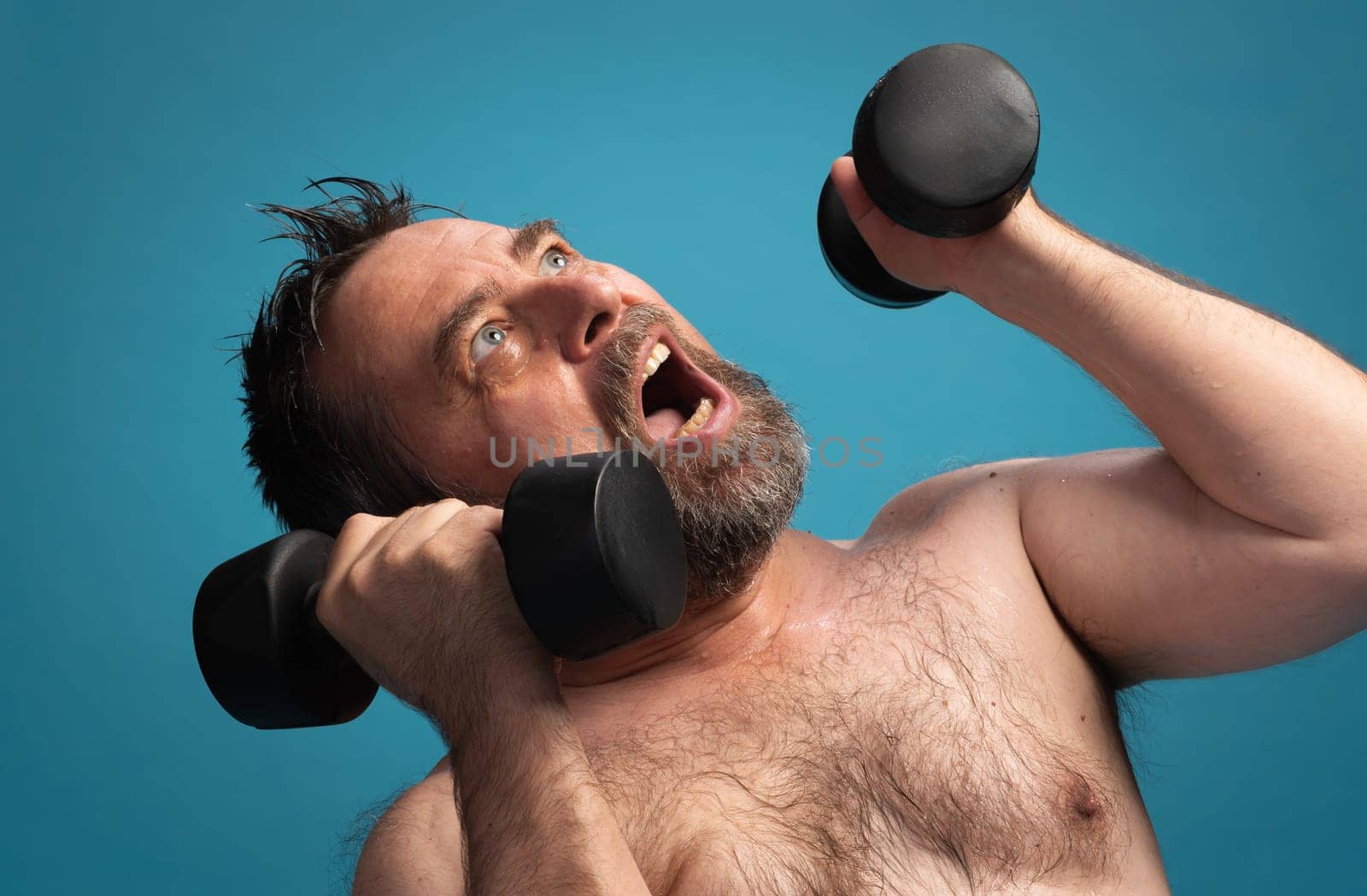 An elderly man lifts dumbbells in an effort-filled workout. He shows determination and focus while exercising. The bright background highlights his commitment to fitness and health.