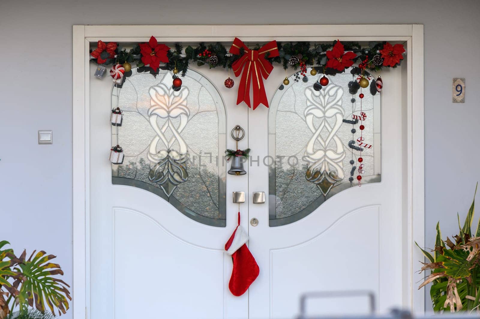 Bright red poinsettias and garlands frame a welcoming entrance with a Christmas stocking hanging below.