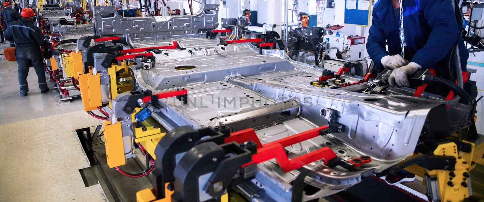 In a bustling manufacturing facility, workers meticulously assemble a vehicle chassis using advanced tools and techniques