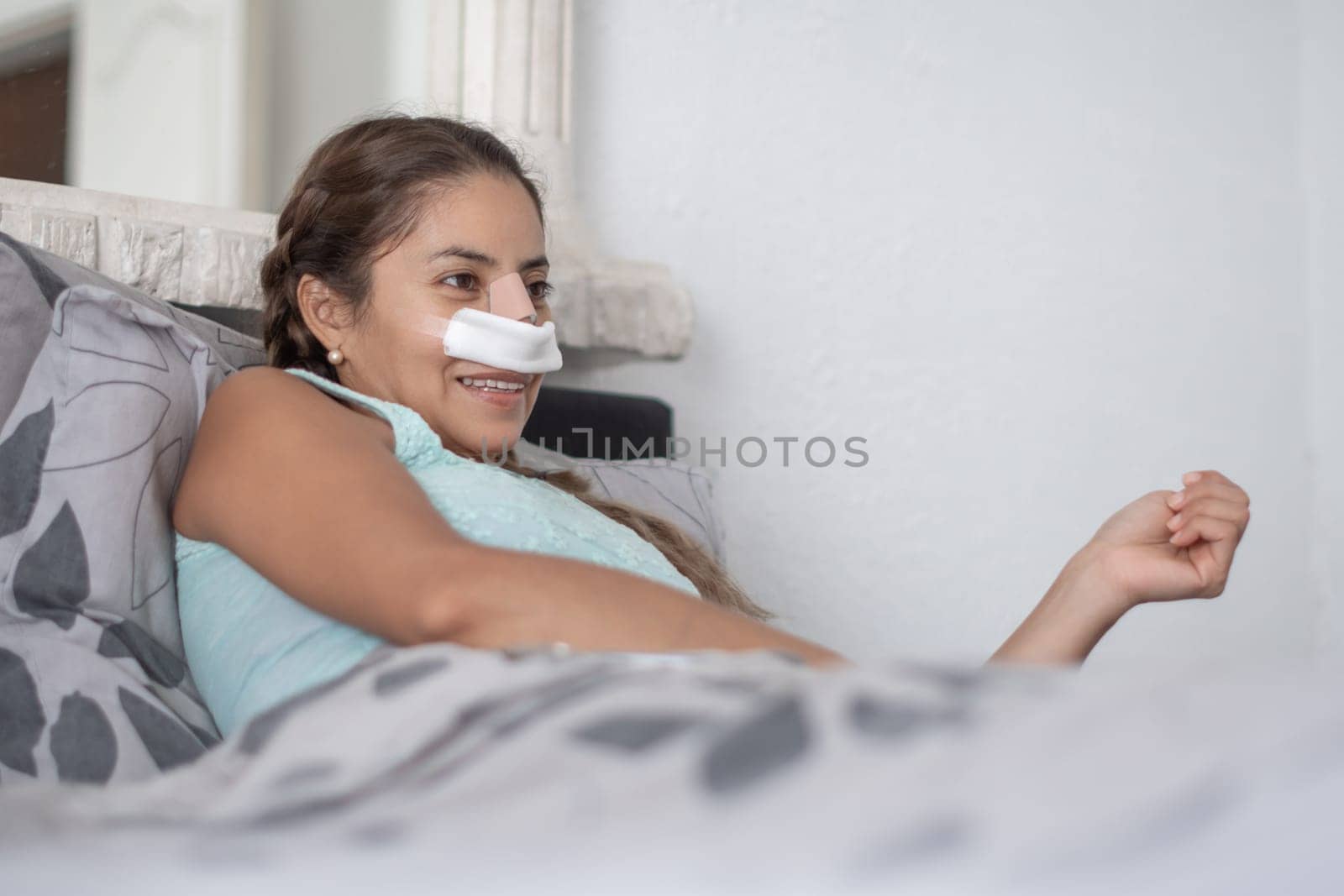 woman lies in bed in casual clothes and with bandages on her face after plastic surgery on her nose, worried and anxious about the result,