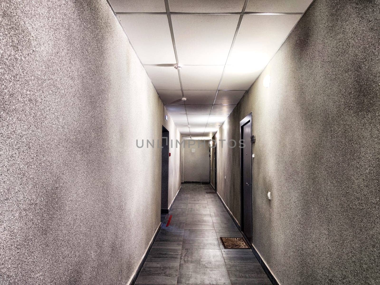 A long, narrow corridor features gray walls, tiled flooring, and multiple closed doors along its length.