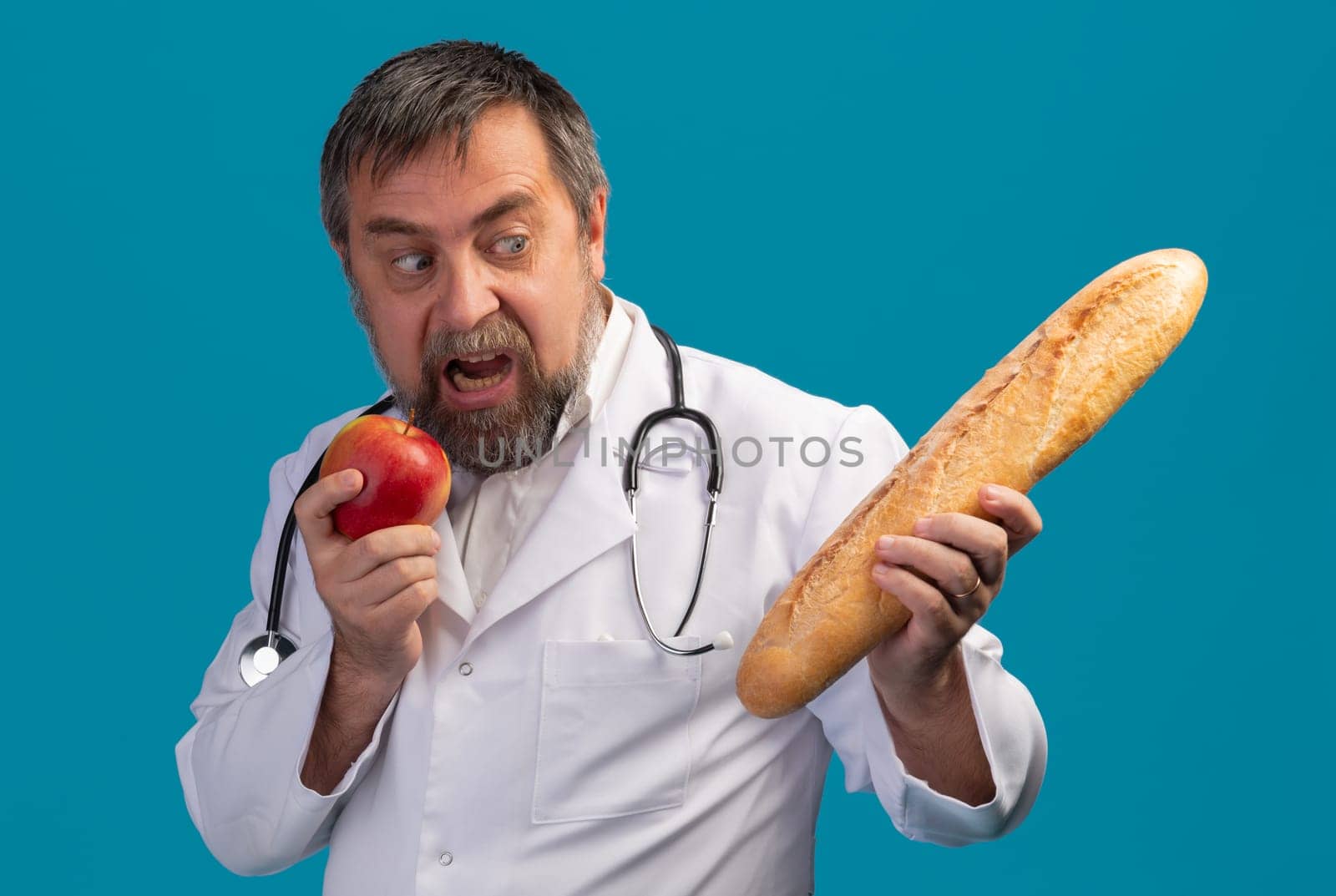 A man in a white lab coat and stethoscope holds a red apple in one hand while looking excitedly at a long baguette in the other.