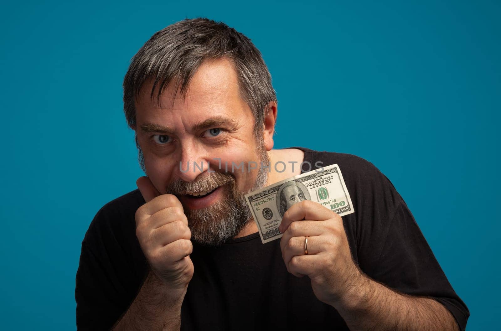 A man with a beard and short hair displays a joyful expression while holding a dollar bill. He gives a thumbs-up gesture, surrounded by a solid blue backdrop.