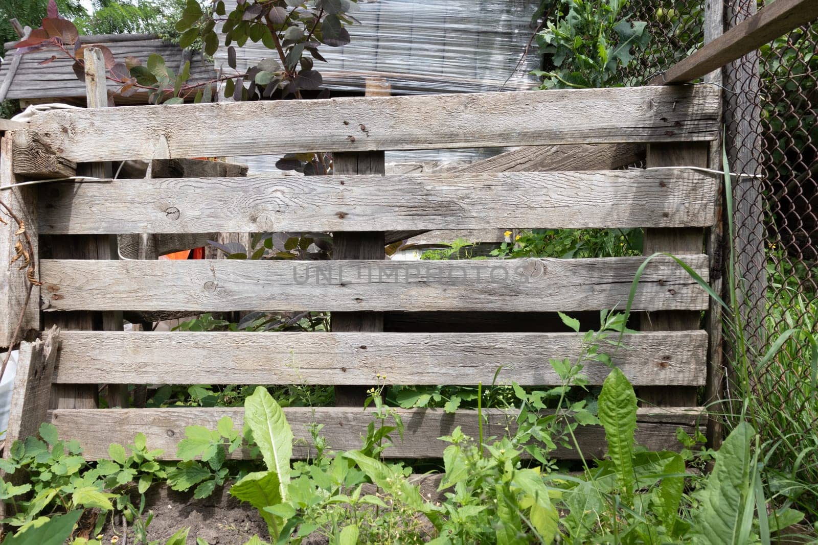 A rustic wooden fence with weathered planks and natural grain patterns, surrounded by greenery in an outdoor environment.