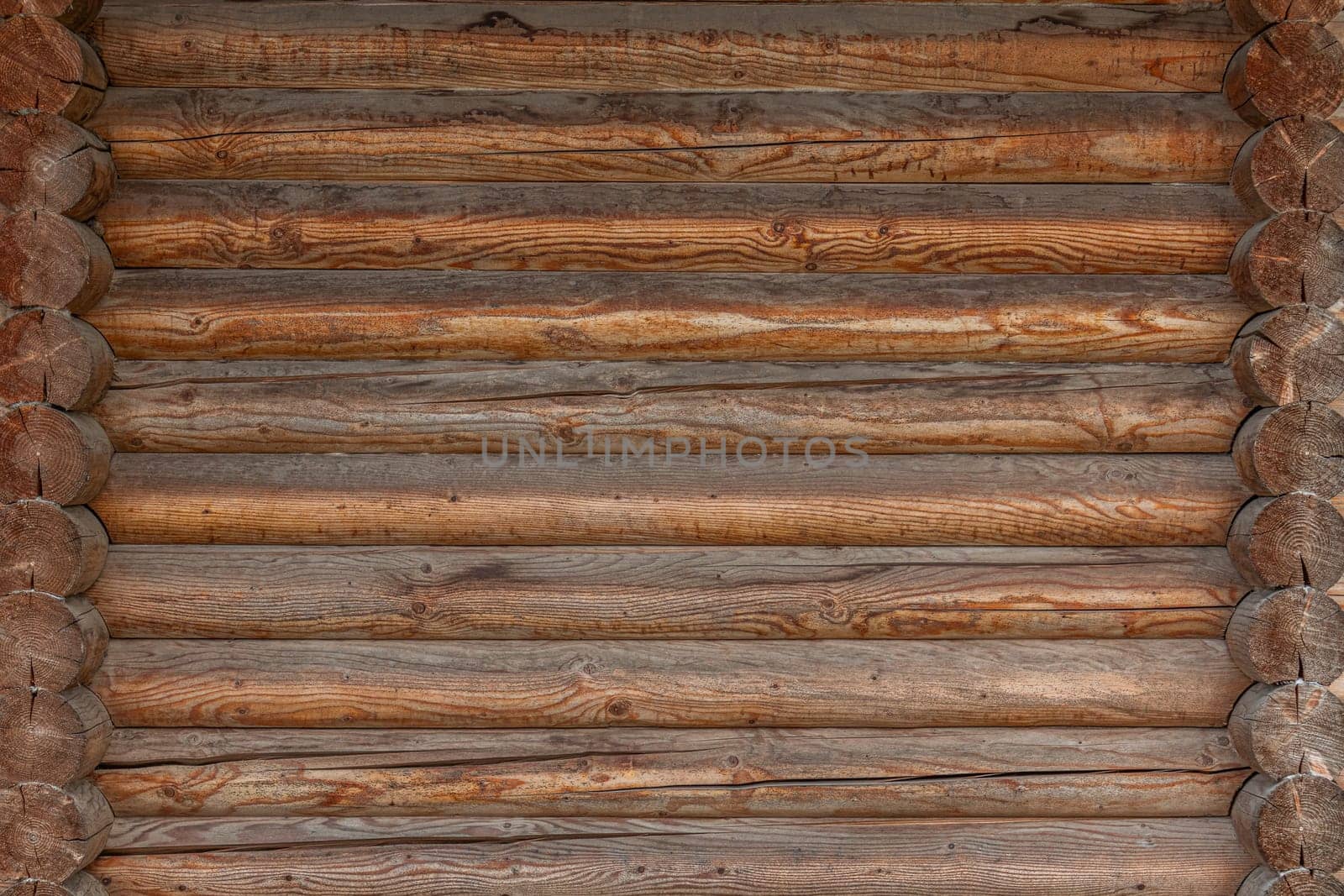 A close-up view of a log cabin wall featuring horizontally aligned wooden logs with visible grain, rough textures, and a warm rustic appearance.