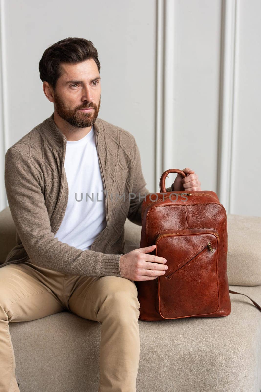 A fashionable man sits with a yellow brown backpack in a contemporary room, embodying urban style and professionalism.