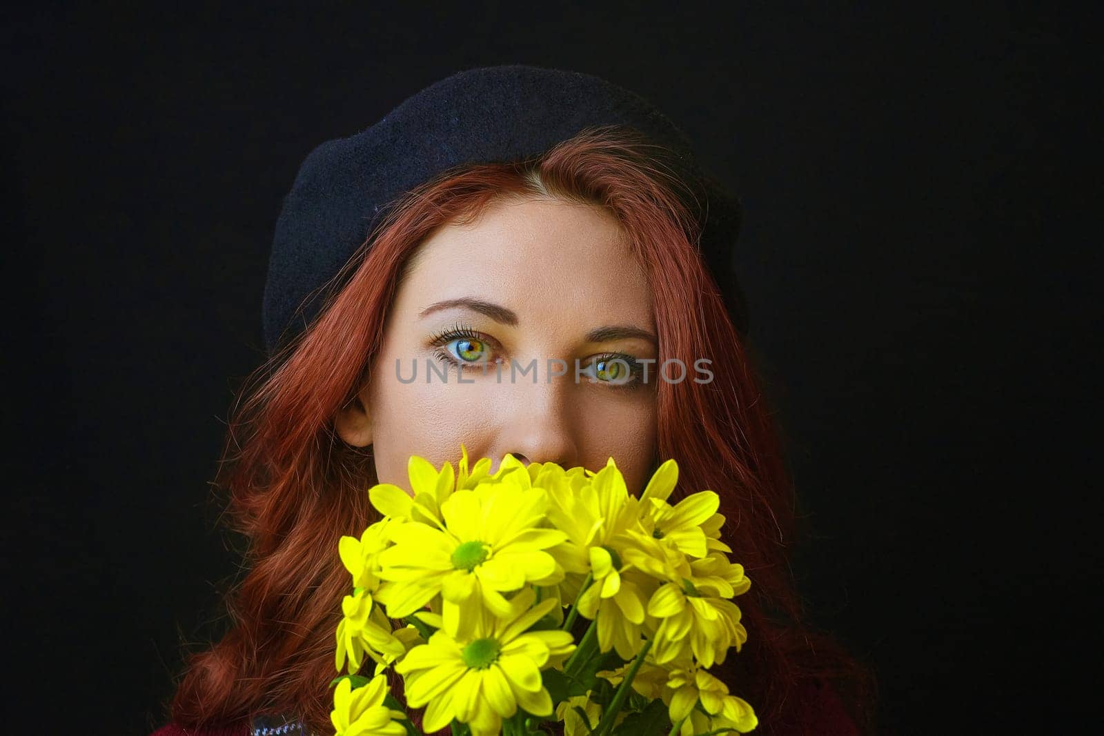 French redhead woman in black beret holds and sniffs yellow chrysanthemums