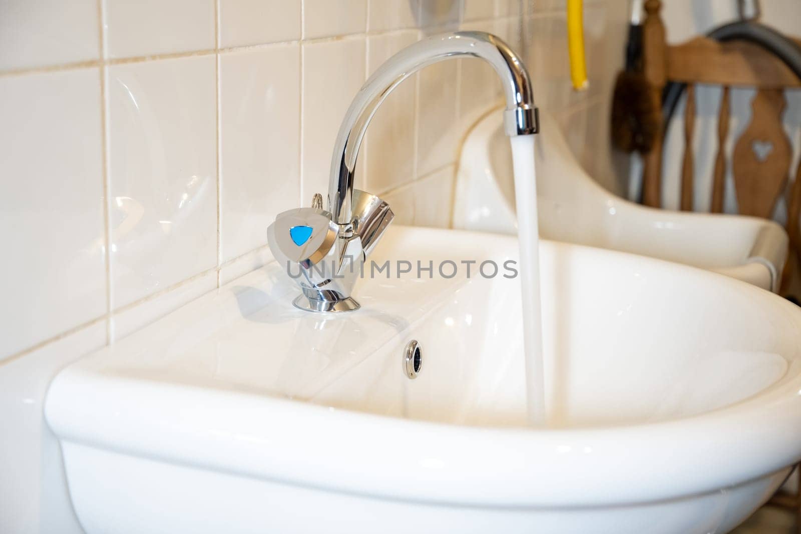 Flowing water from a shiny chrome faucet into a white sink, tiled wall background, clean and modern design concept,