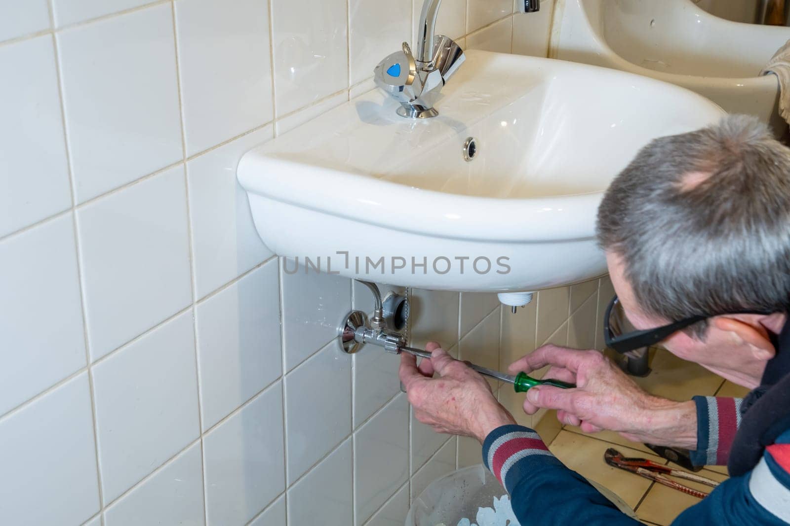 Hands of owner using wrench to repair sink in tiled bathroom, DIY sink installation concept at home,