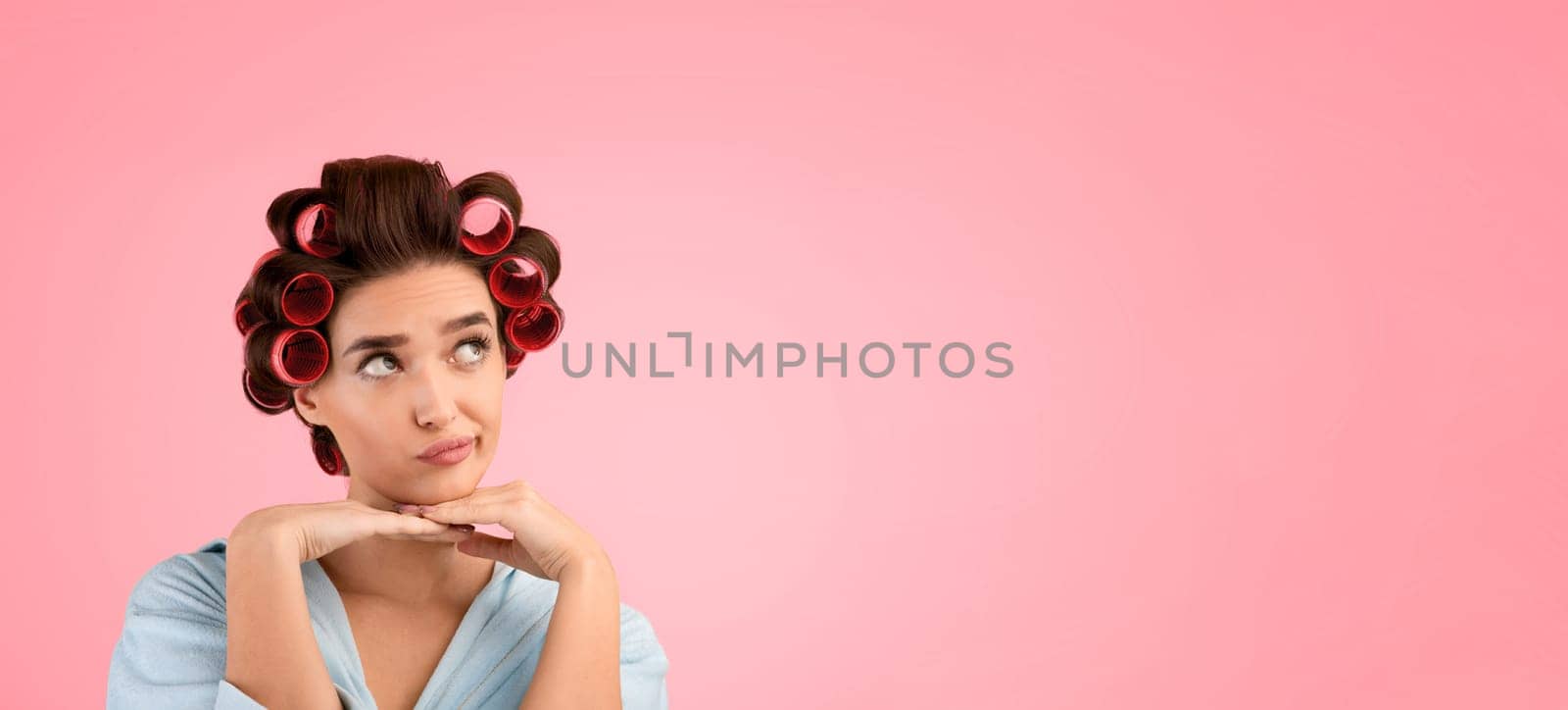 Thoughtful Female With Hair Curlers Thinking Holding Hands Near Face Looking Aside At Copy Space Over Yellow Studio Background. Beauty Care And Cosmetics Advertisement. Housewife's Thoughts