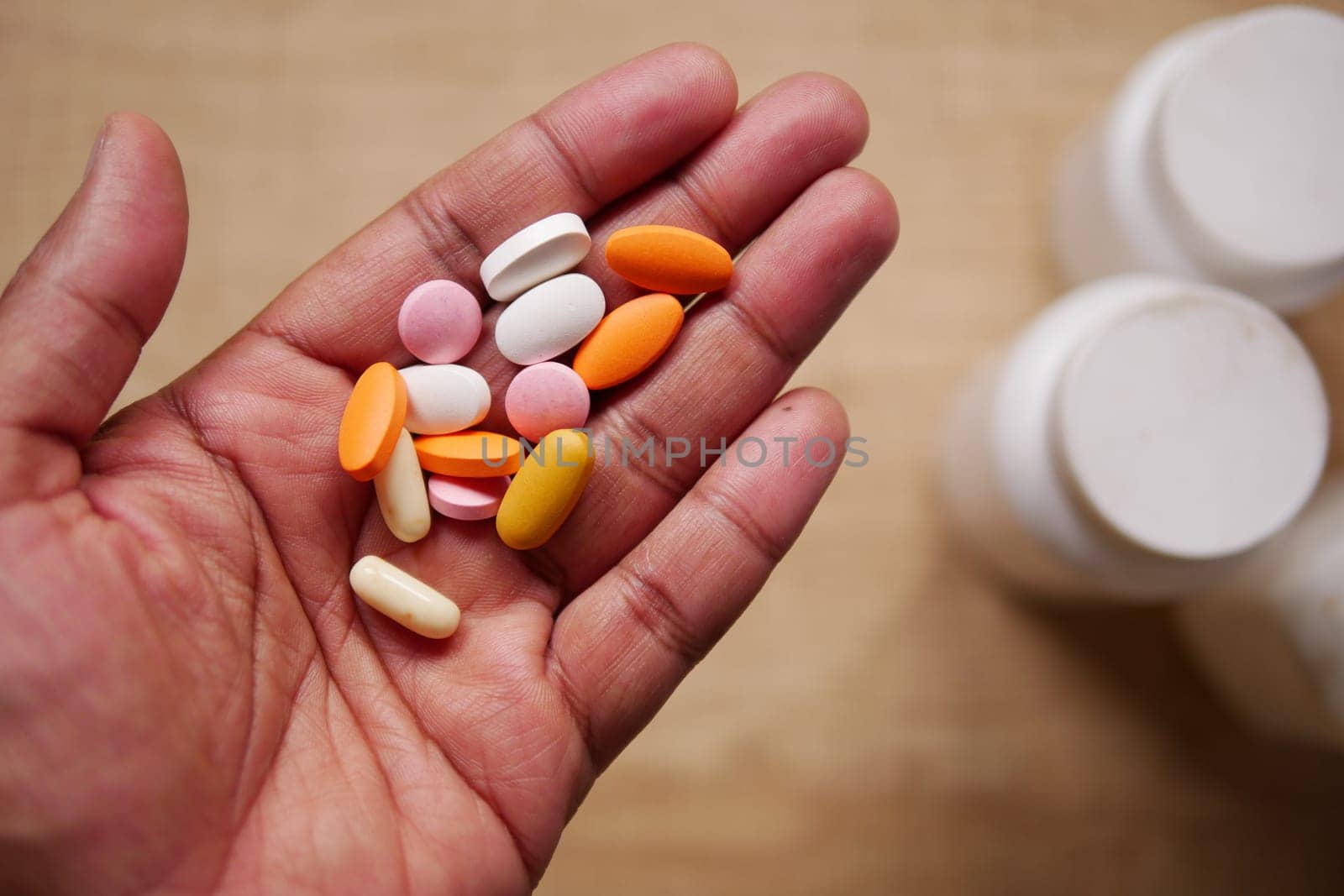 A hand is holding a collection of various colorful dietary pills and nutritional supplements