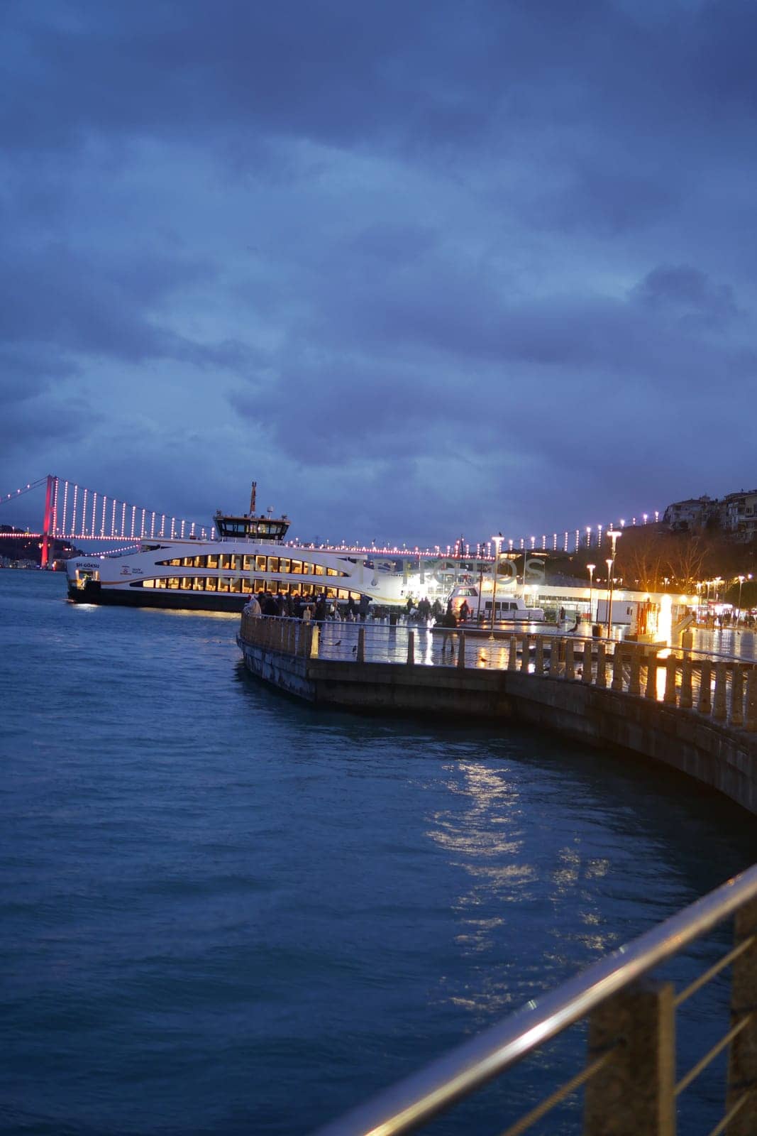 The serene waterfront view at dusk shows city lights reflecting on the calm water