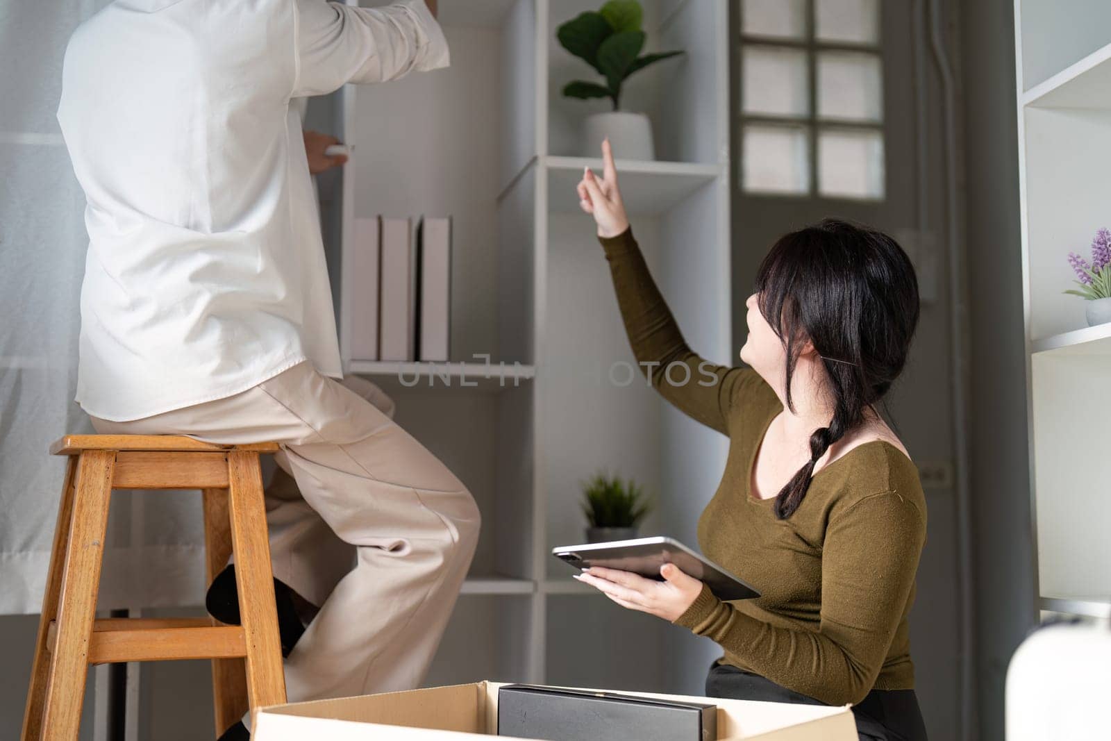 A couple joyfully sets up their new home arranging shelves and sharing ideas in a bright inviting living room.