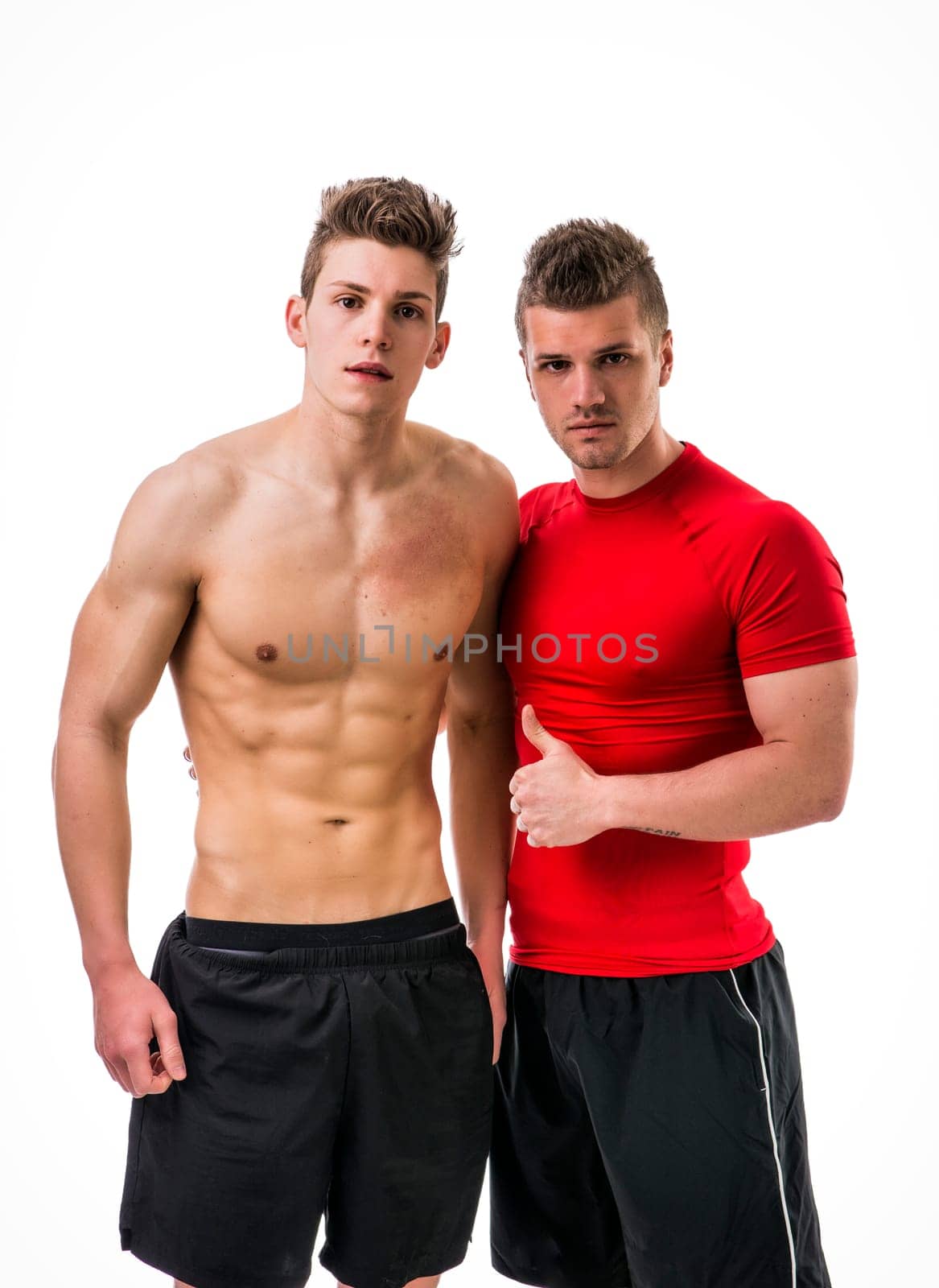 Two young men standing next to each other. The personal trainer is next to his client. Studio shot isolated on white
