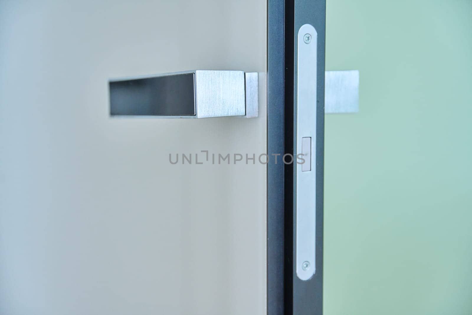 Close-up of a chrome modern door handle on a white glossy door by VH-studio