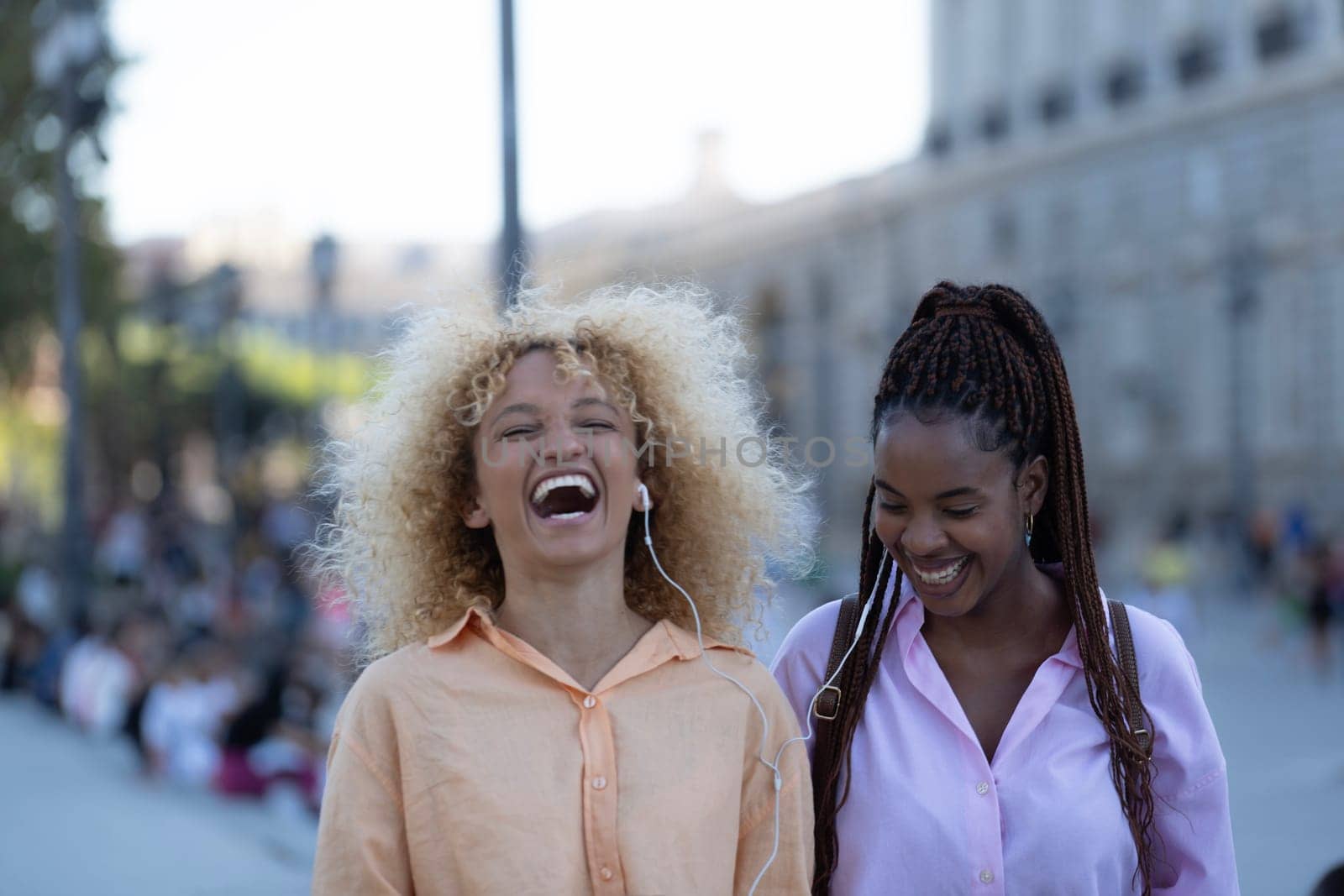 Portrait of happy women friends laughing while walking in Madrid city.