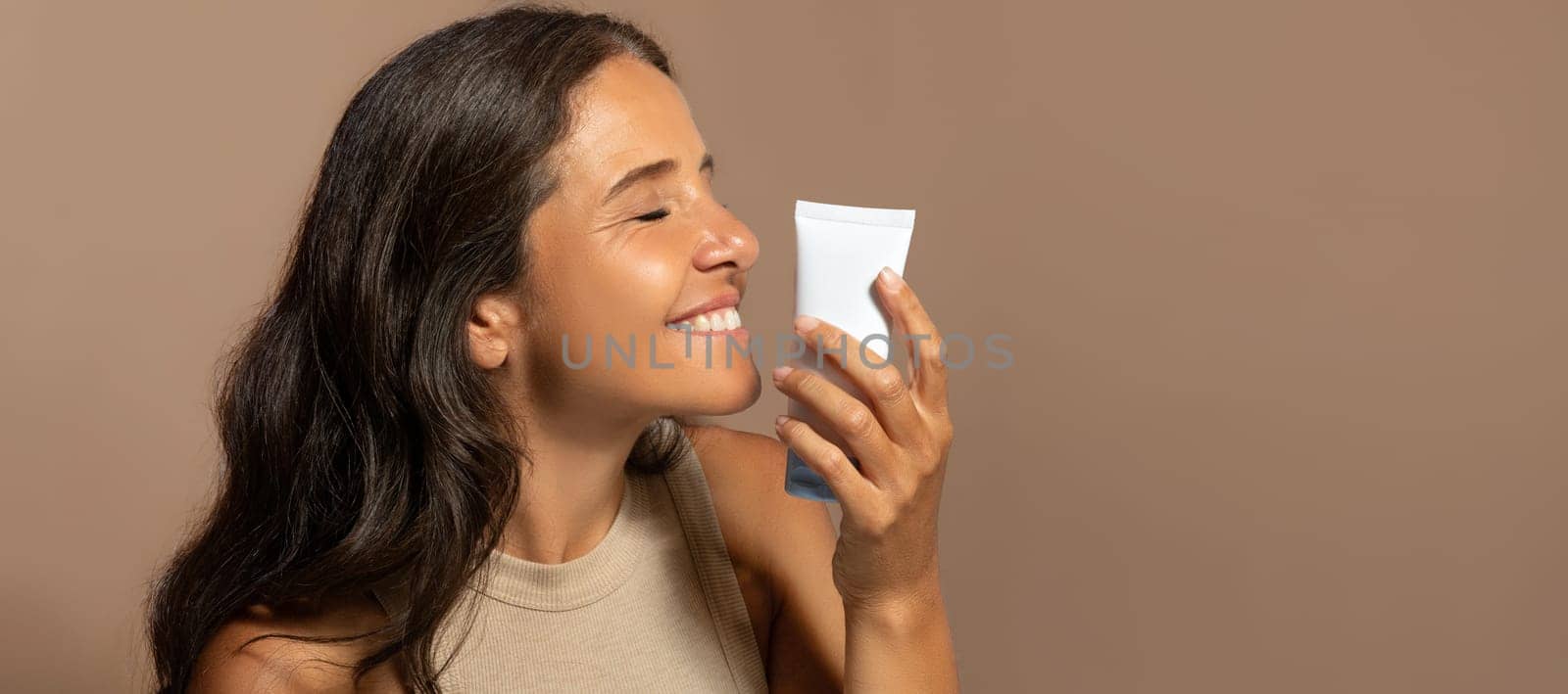 Smiling caucasian elderly woman hold jar of cream, enjoy natural cosmetics, isolated on beige studio background. Beauty care, lifestyle, anti-wrinkle treatment, routine and spa procedures