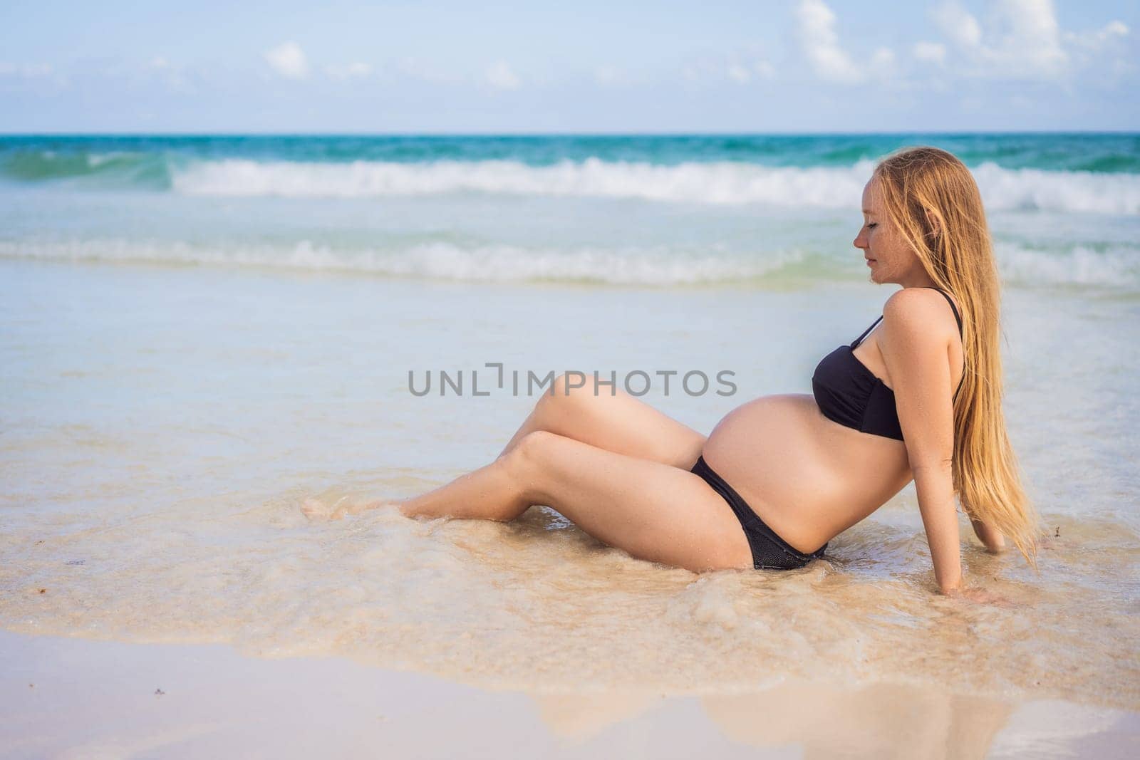 Radiant pregnant woman in a swimsuit, amid the stunning backdrop of a turquoise sea. Serene beauty of maternity by the shore.