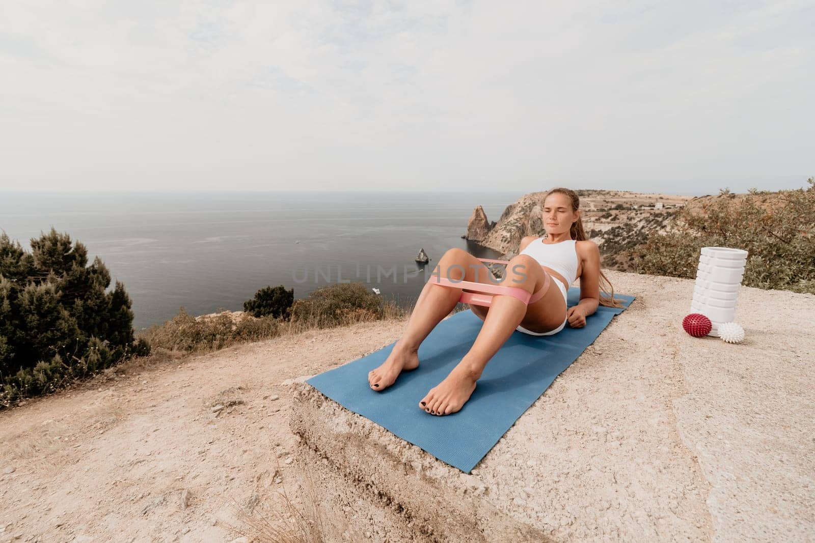 Woman sea pilates. Sporty, middle-aged woman practicing pilates in park near the sea. trains on a yoga mat and exudes a happy and active demeanor. healthy lifestyle through exercise and meditation. by panophotograph