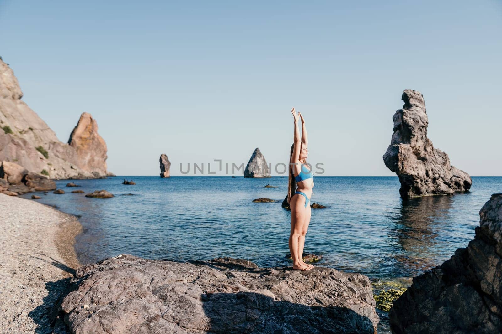 Middle aged well looking woman with black hair doing Pilates with the ring on the yoga mat near the sea on the pebble beach. Female fitness yoga concept. Healthy lifestyle, harmony and meditation.