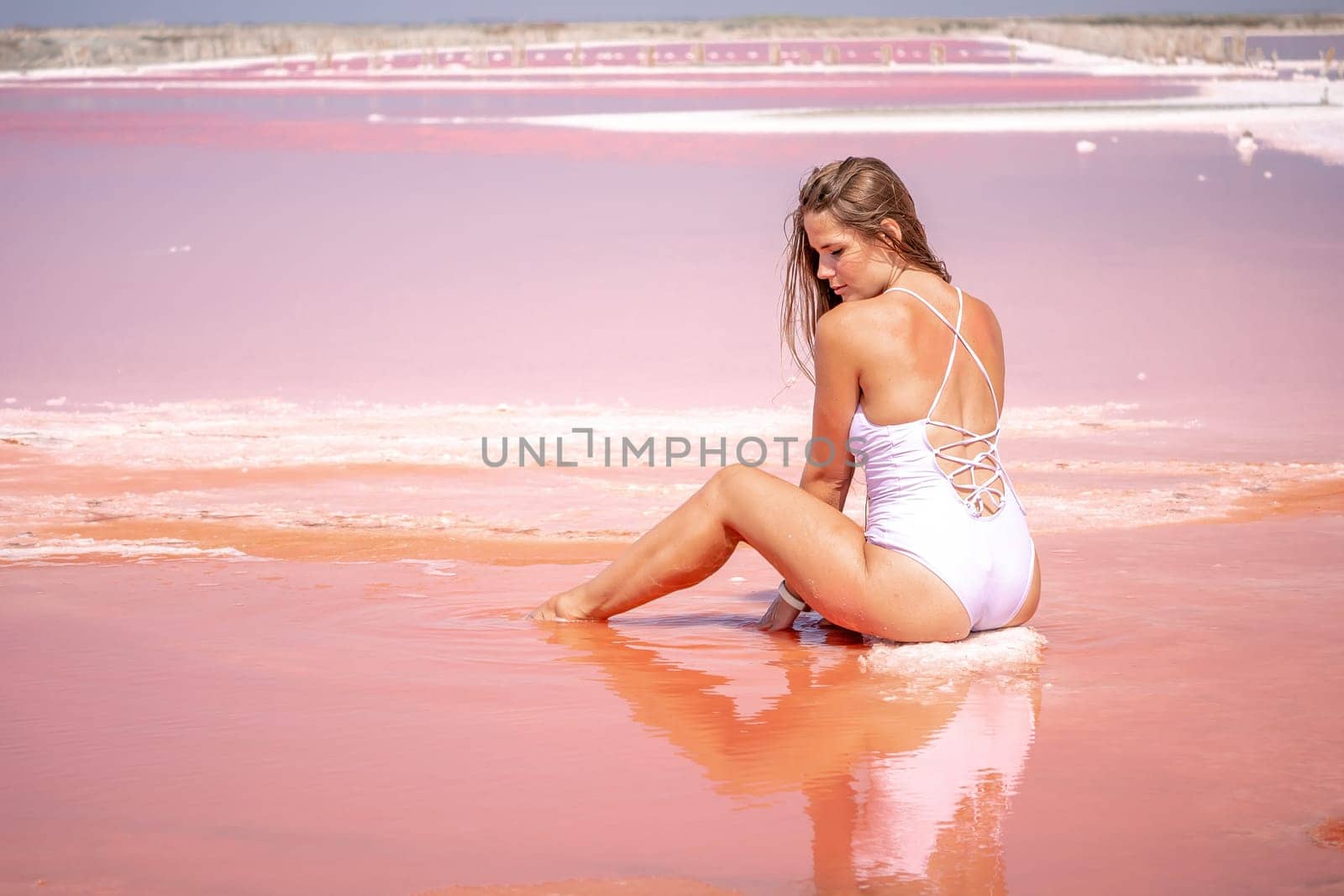 Young woman with long hair in pink salty lake with crystals of salt. Extremely salty pink lake, colored by microalgae with crystalline salt depositions. Spa, beauty and health care concept. by panophotograph