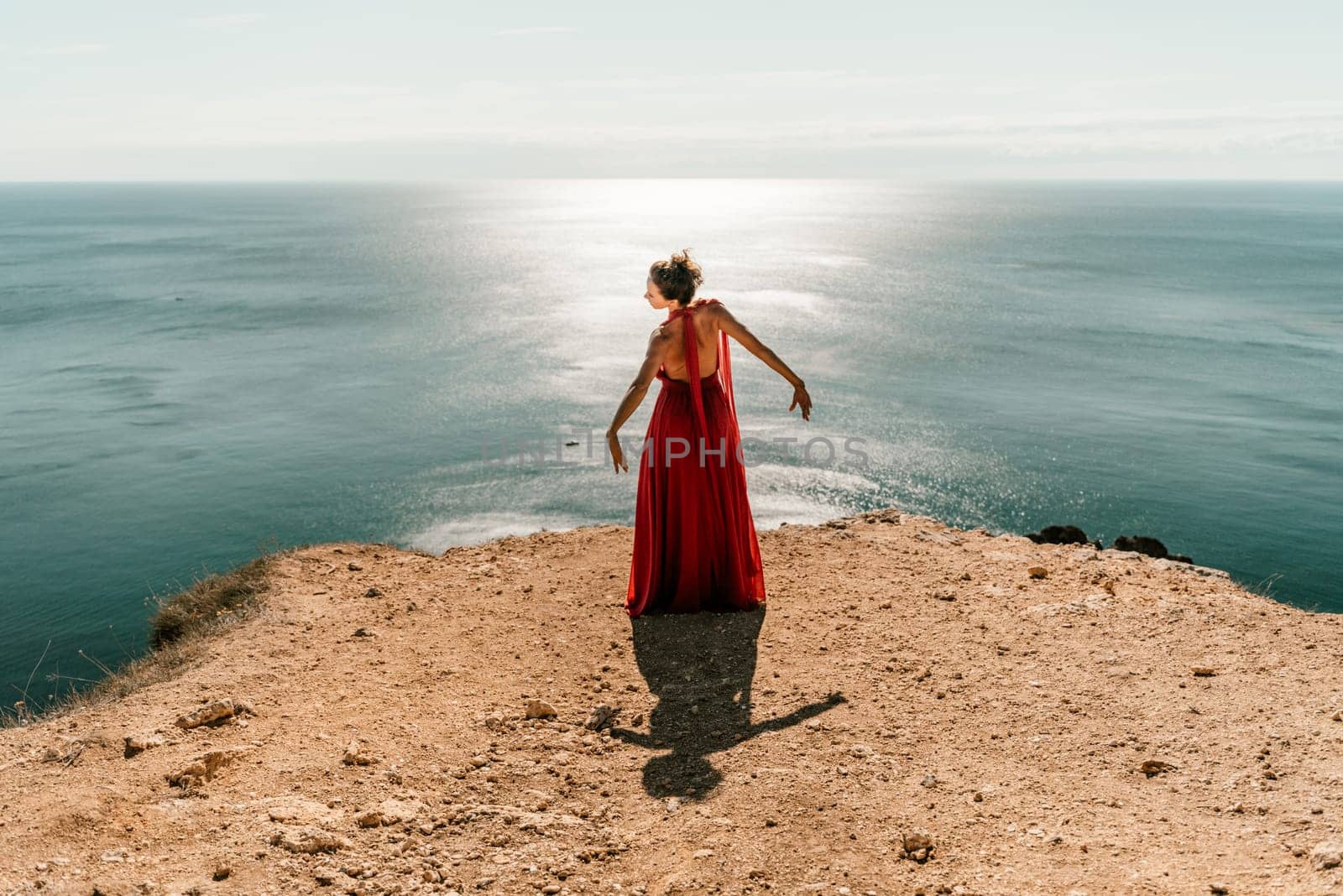 Woman red dress sea. posing on a rocky outcrop high above the sea. Girl on the nature on blue sky background. Fashion photo