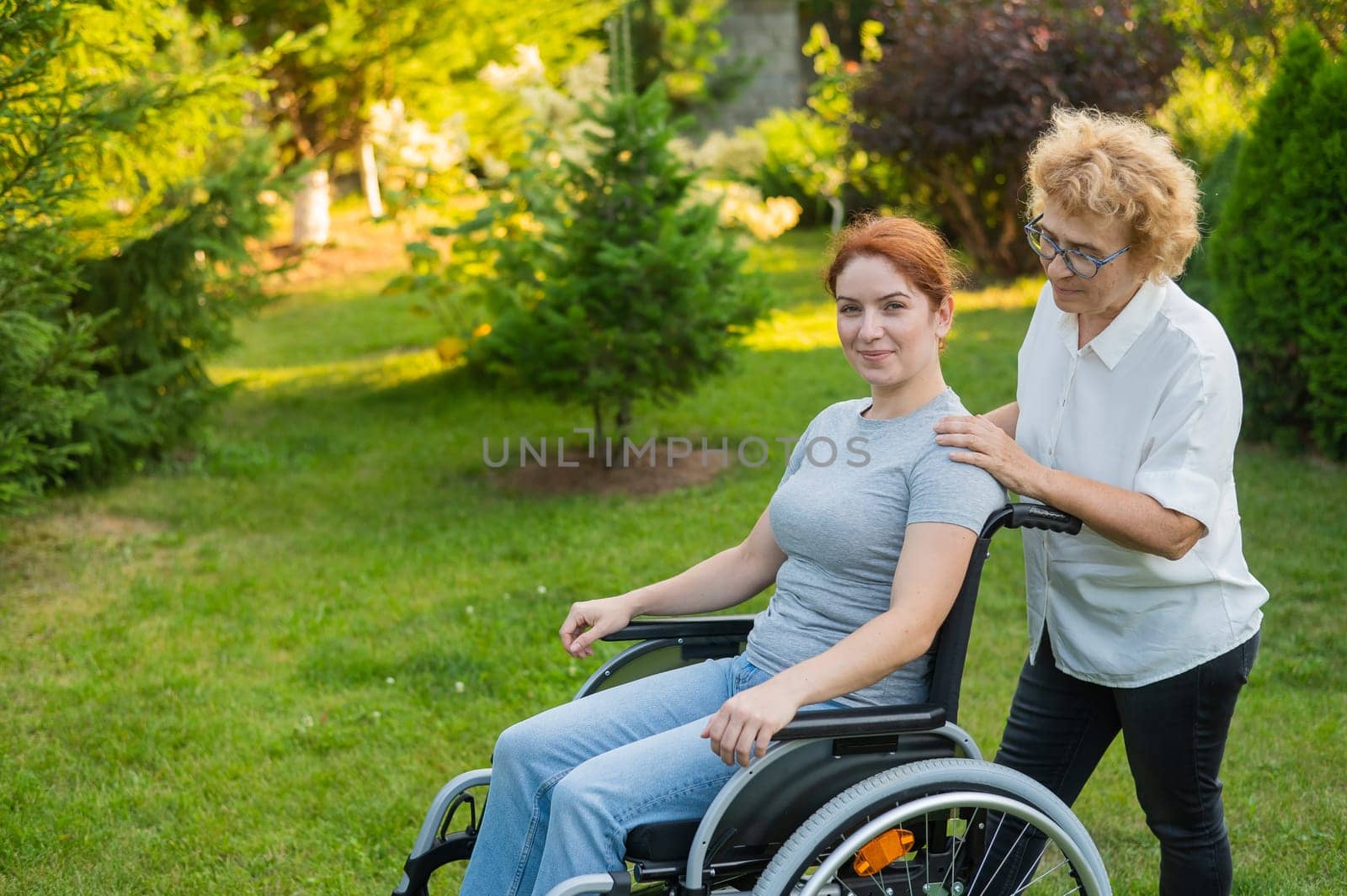 An elderly woman is carrying an adult daughter sitting in a wheelchair. Walk outdoors. by mrwed54