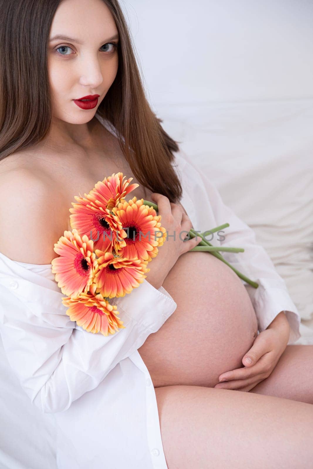 A stunningly beautiful pregnant model gracefully holding vibrant flowers, all captured in a soft, serene setting