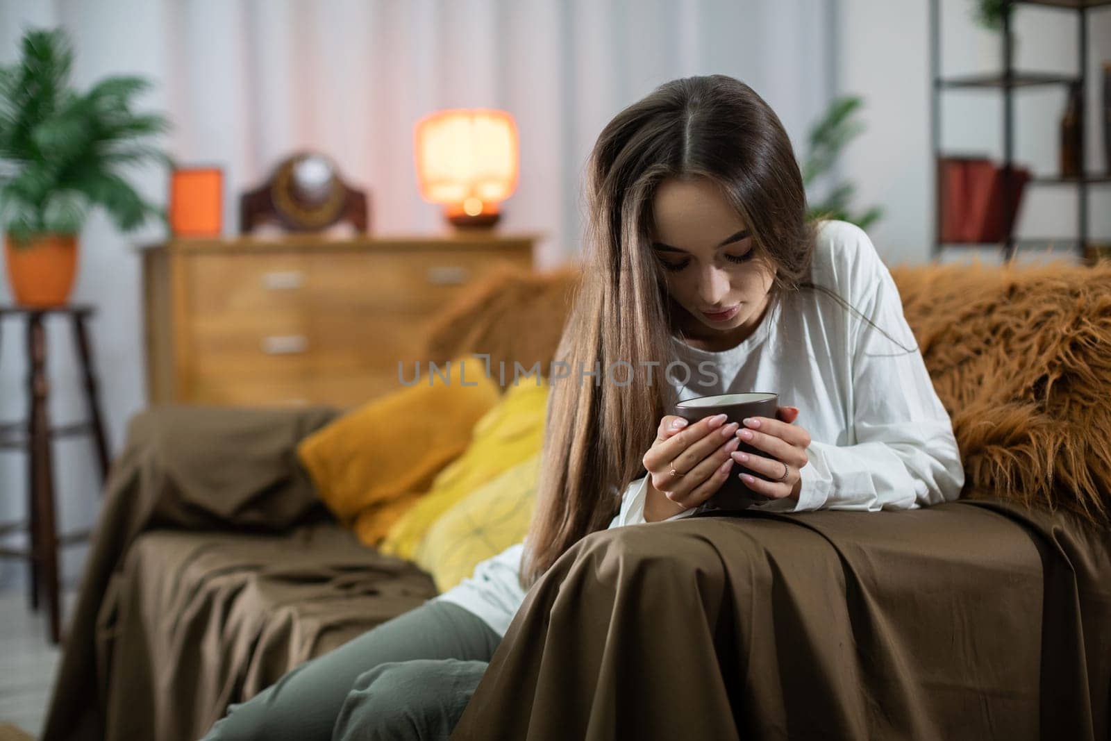 In a warm and inviting living room atmosphere, a young woman intently focuses on her smartphone device