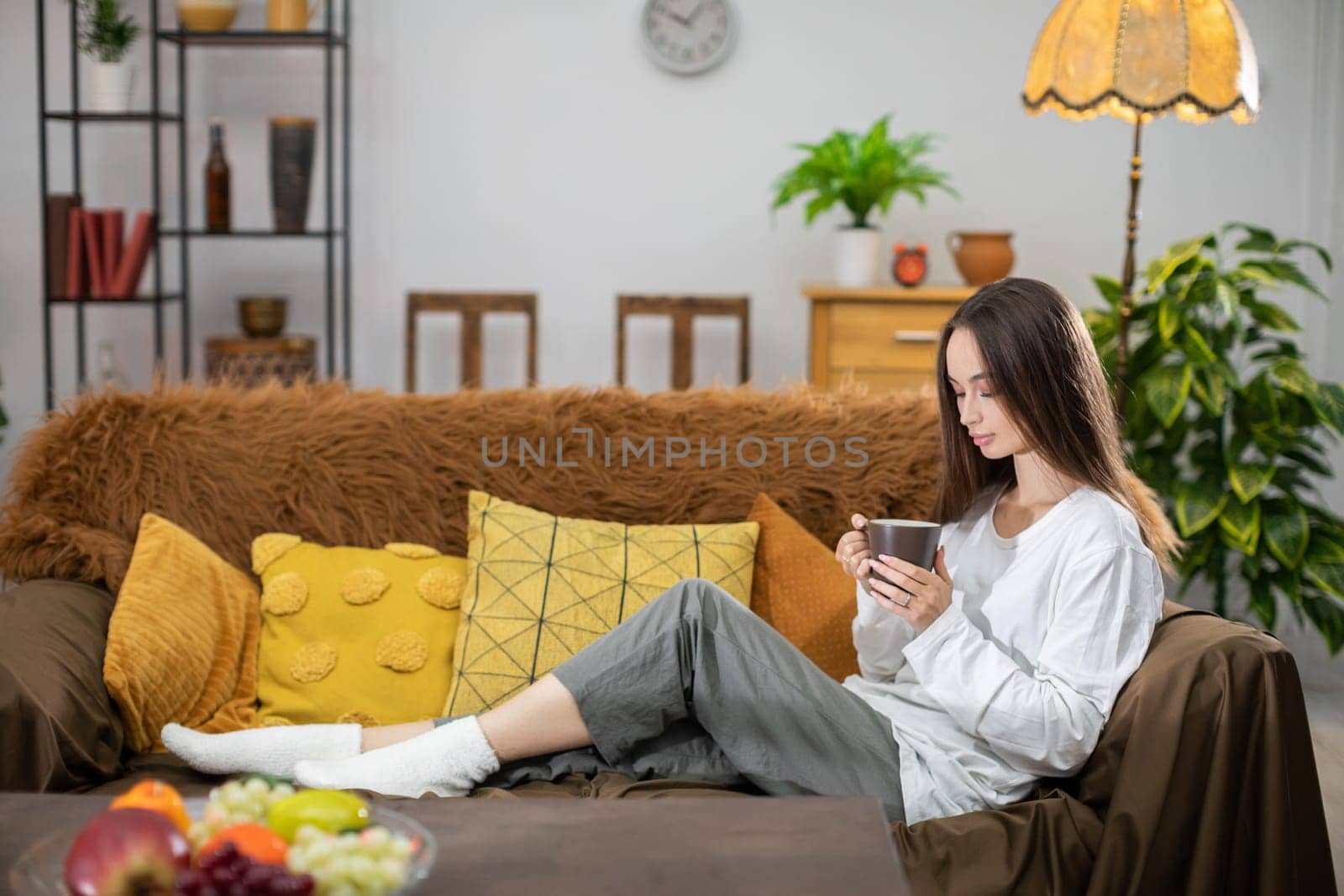A woman is peacefully relaxing on a couch while enjoying a warm cup of coffee in her stylish, cozy living room