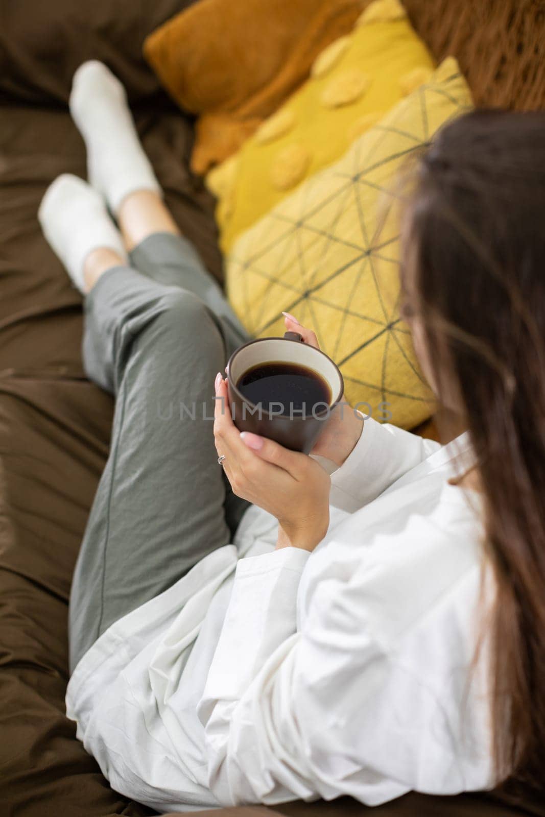 A serene individual finds joy in sipping a warm cup of coffee while relaxing comfortably on a cozy couch
