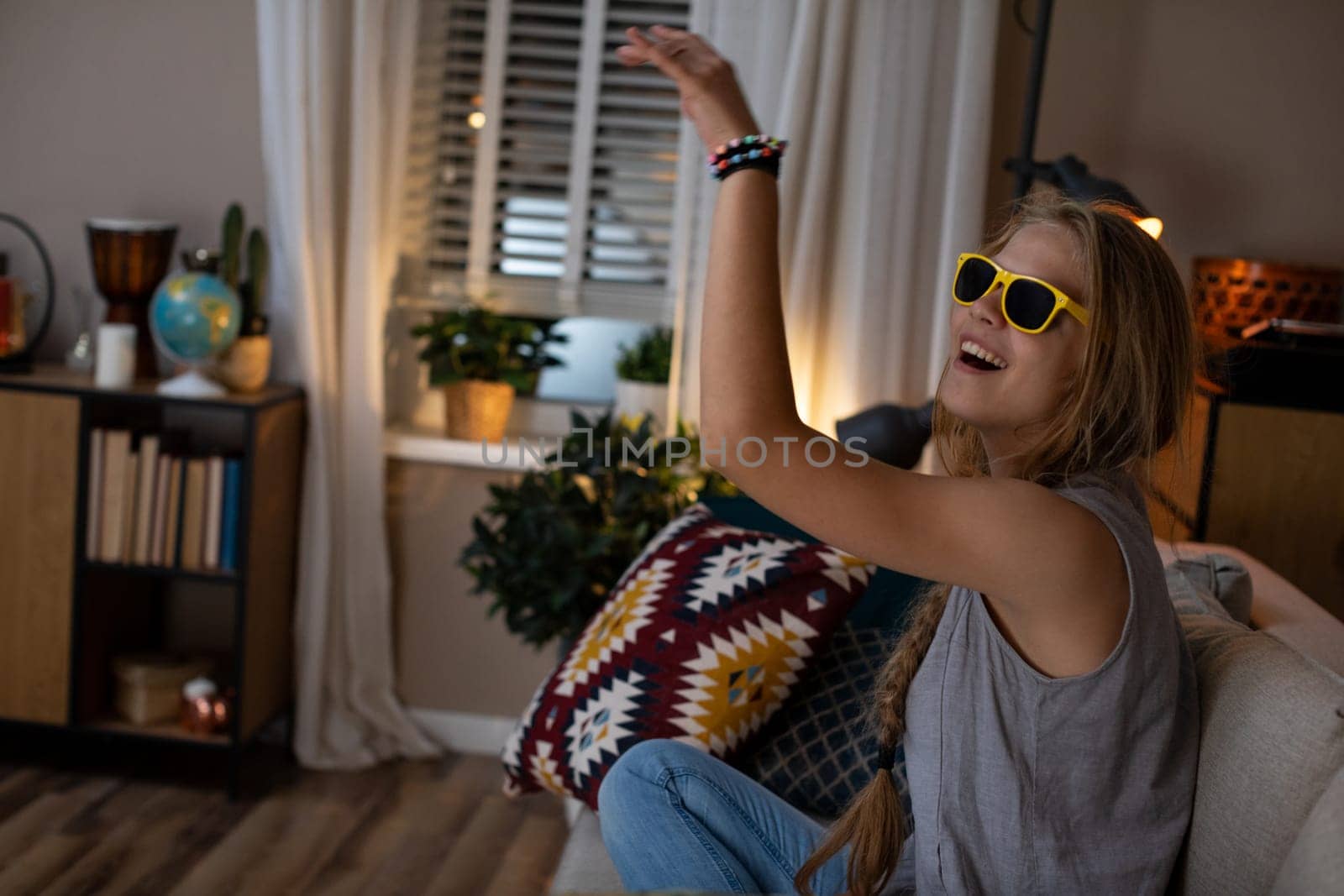 A young woman is having fun dancing to music at home, wearing stylish sunglasses and expressing her joy
