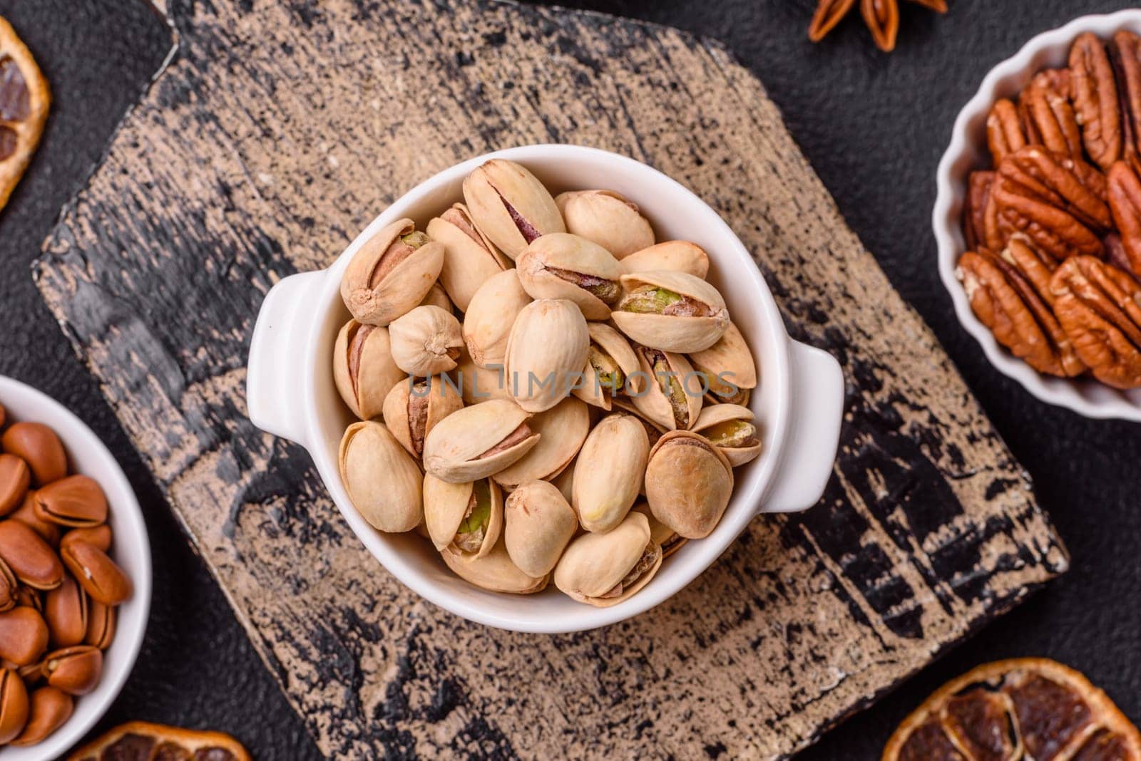 Delicious nutritious pistachio nuts in ceramic bowl on dark concrete background