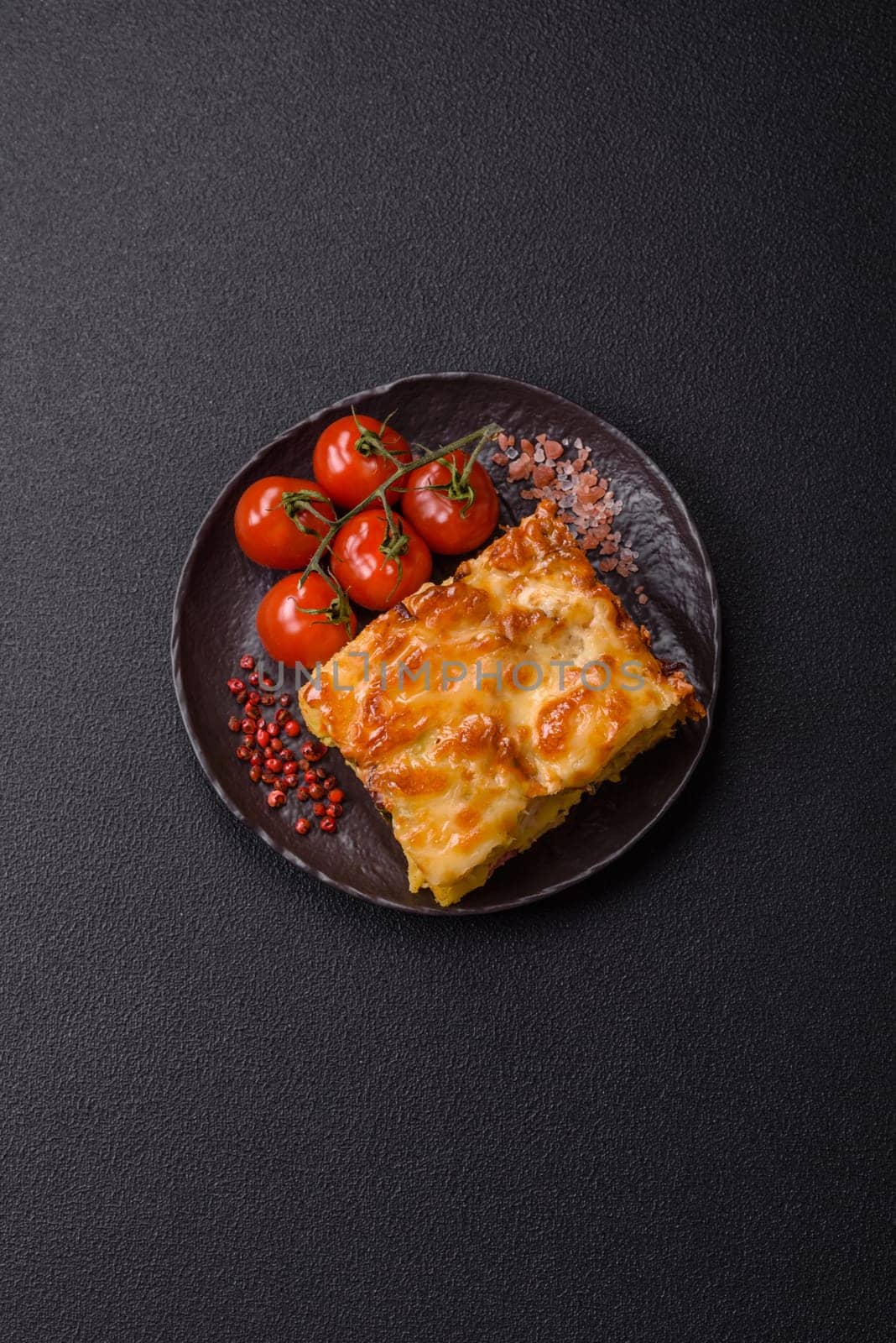 Lasagna or pasta layered with meat, cheese, salt, spices and herbs on dark concrete background