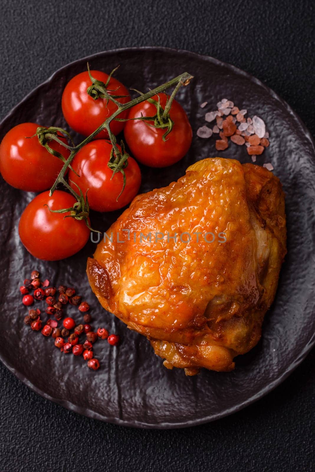 Delicious juicy chicken thighs baked with salt, spices and herbs in a ceramic plate on a dark concrete background