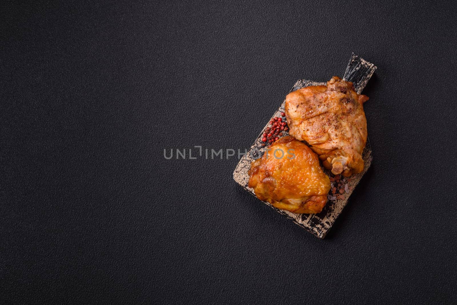 Delicious juicy chicken thighs baked with salt, spices and herbs in a ceramic plate on a dark concrete background