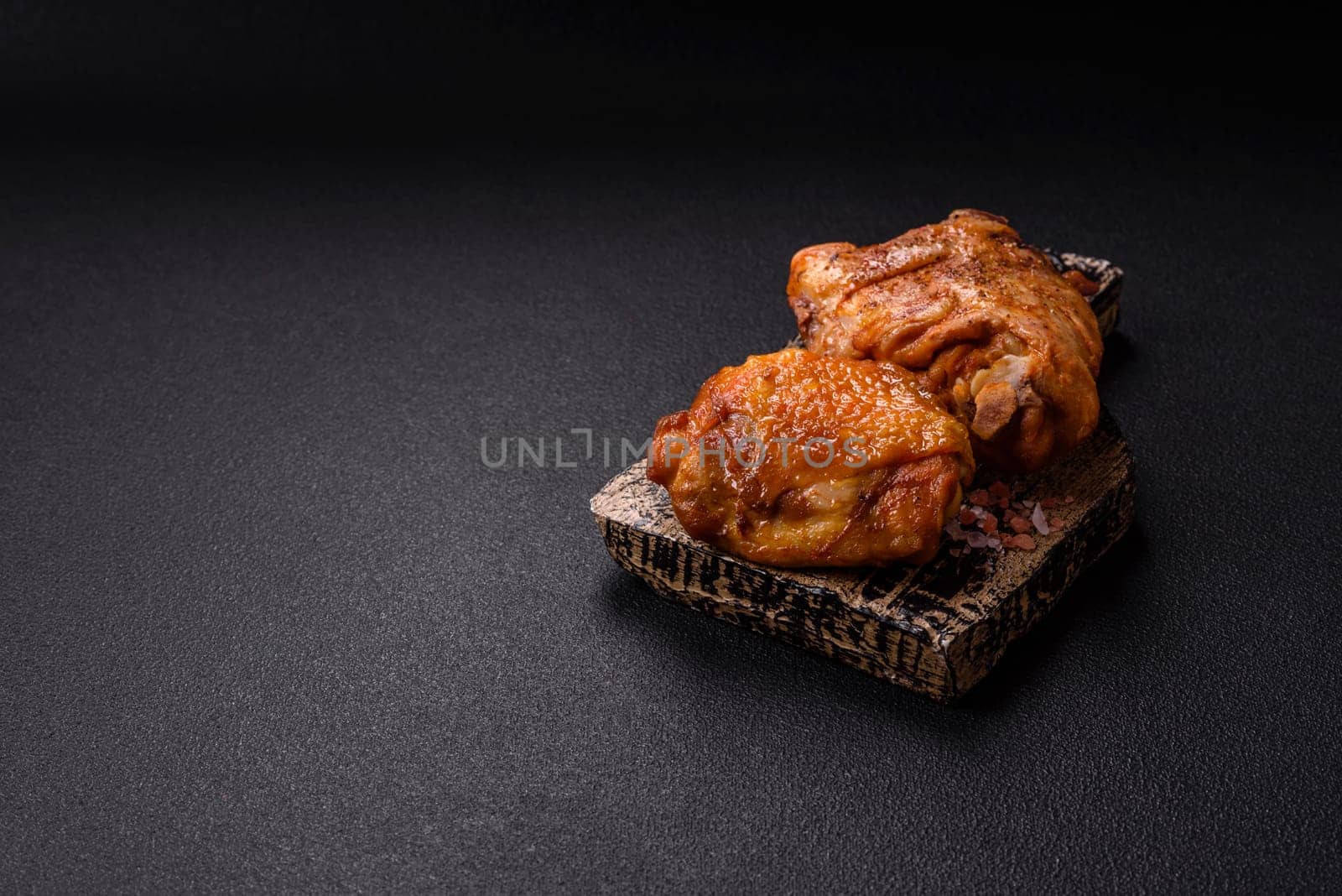 Delicious juicy chicken thighs baked with salt, spices and herbs in a ceramic plate on a dark concrete background