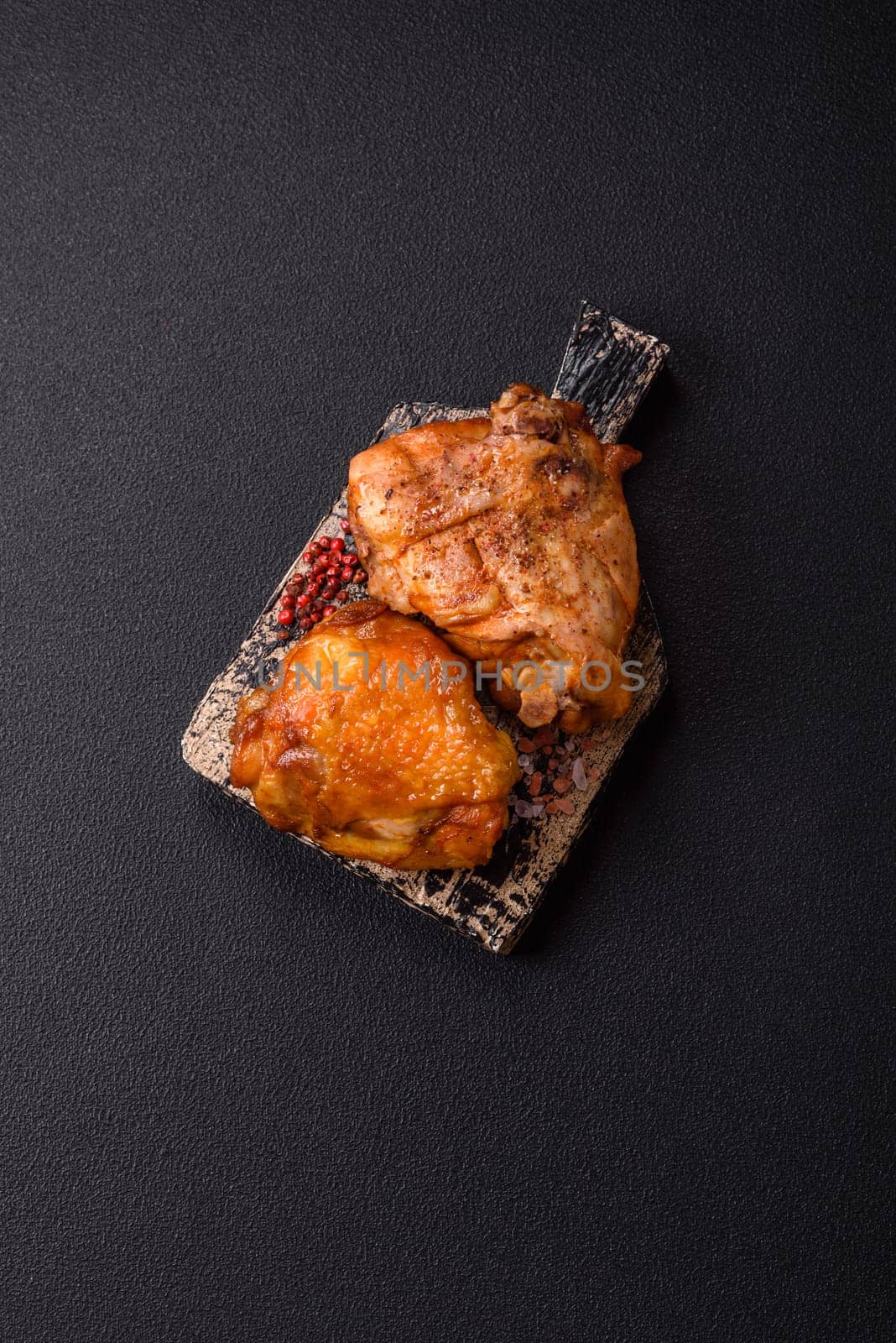 Delicious juicy chicken thighs baked with salt, spices and herbs in a ceramic plate on a dark concrete background